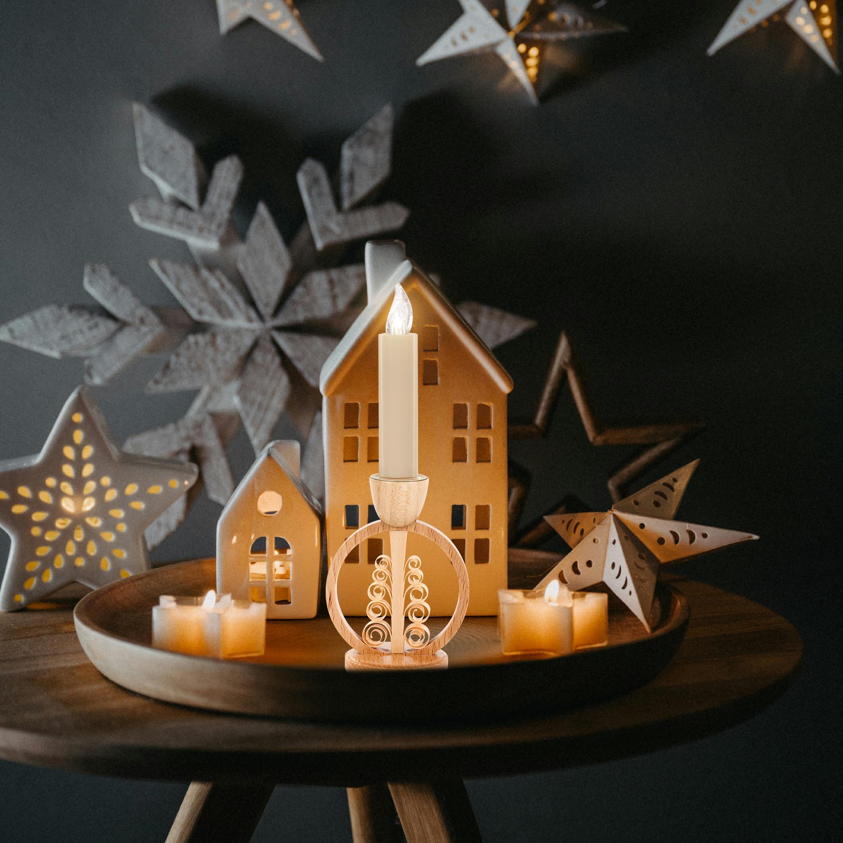 A wooden candle holder in the shape of a spiral tree, set within a circular frame, holding a lit candle atop, surrounded by decorative candle houses.