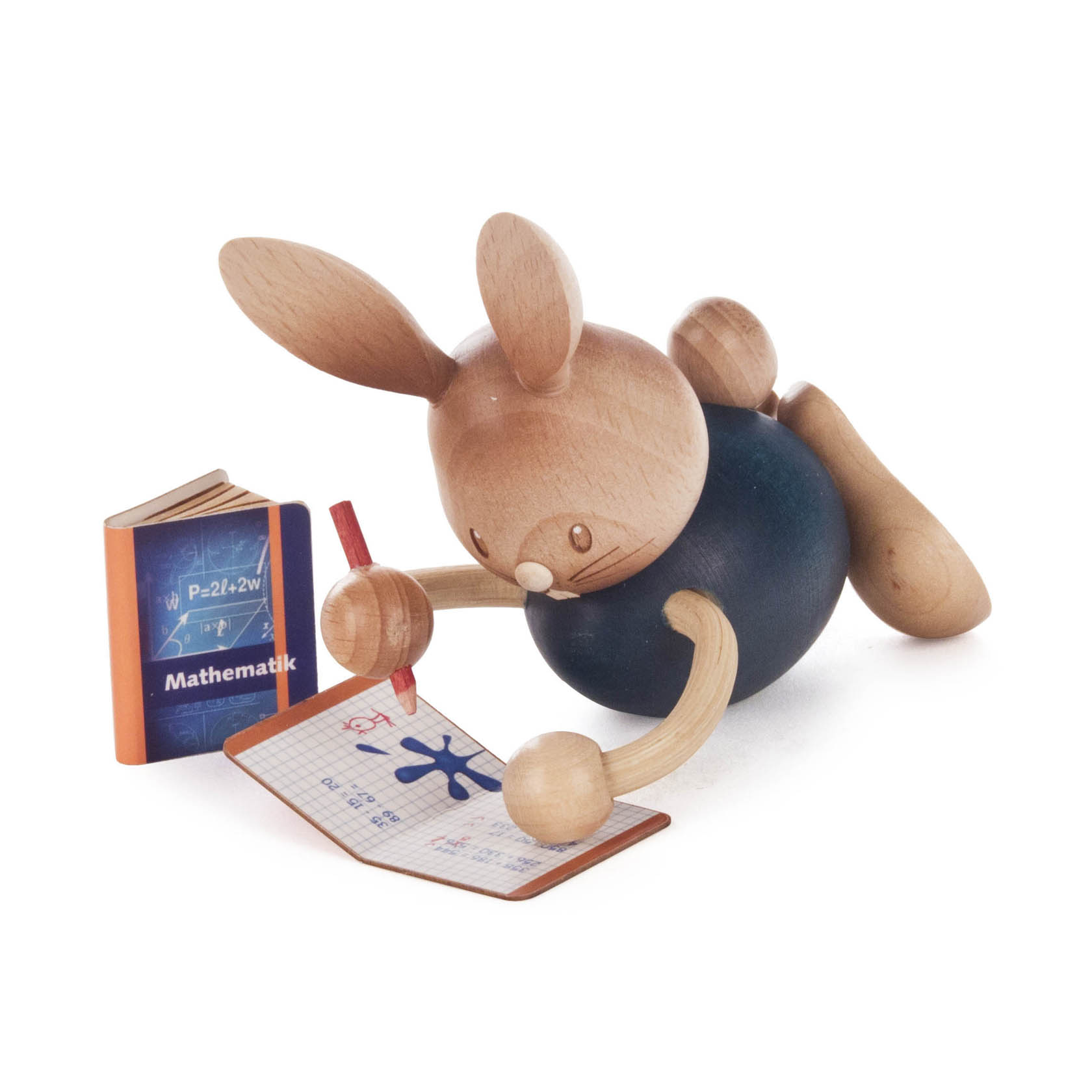 A wooden figure of a rabbit named 'Stupsi' is lying down as if writing in a math exercise book with a red pencil. A math book is propped up nearby. im Dregeno Online Shop günstig kaufen