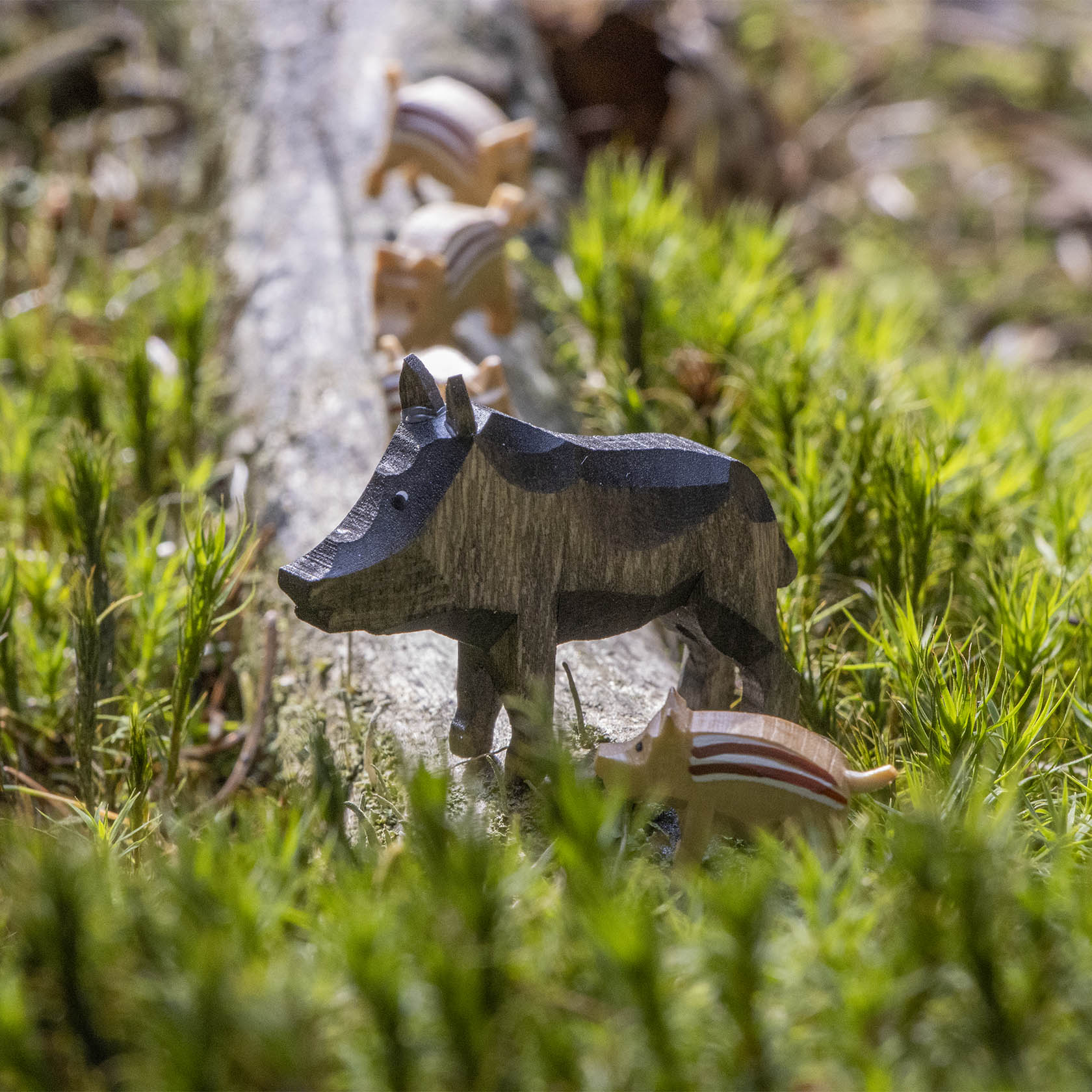 Wooden figurine of a wild boar with four piglets walking in a line on a log, surrounded by grass.