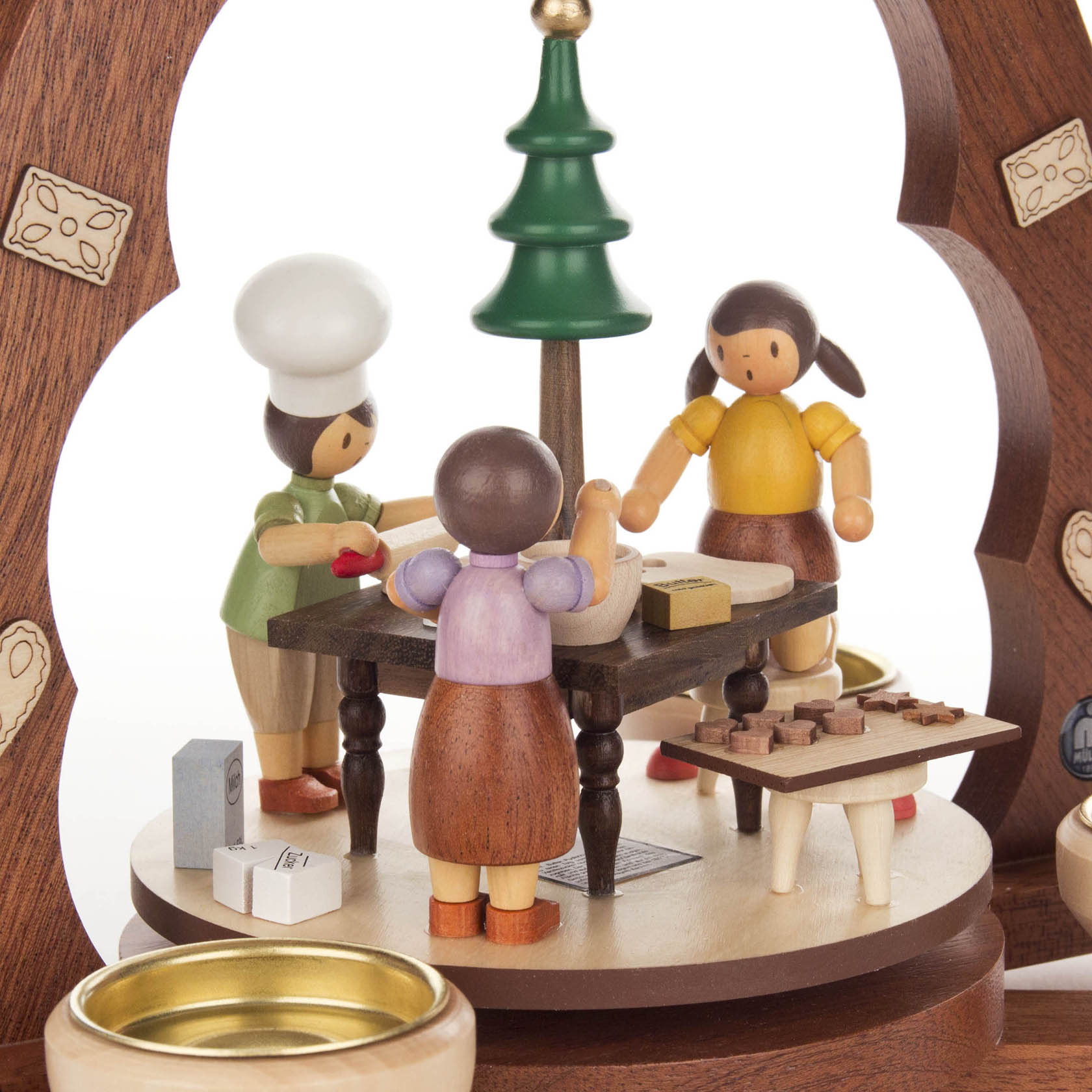 Holzfiguren einer Weihnachtsbäckerei: drei Bäckerinnen um einen Tisch, Teig und Kekse bearbeitend, unter einer Holzpyramide mit Tannenbaum.