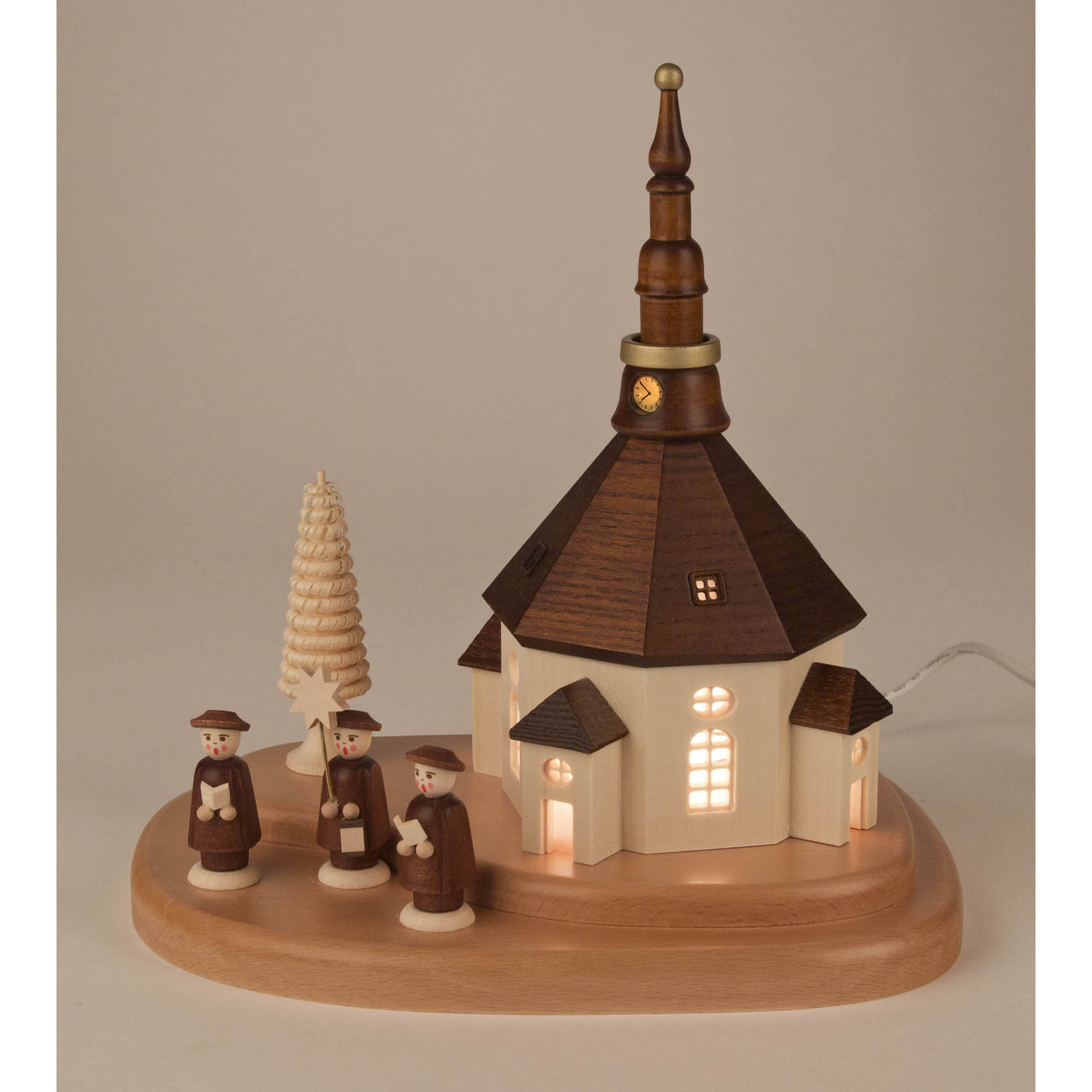 Erzgebirgische Holzschnitzerei: Seiffener Kirche mit beleuchteten Fenstern und vier Kurrendesängern auf einem Holzsockel, daneben ein geschnitzter Baum.