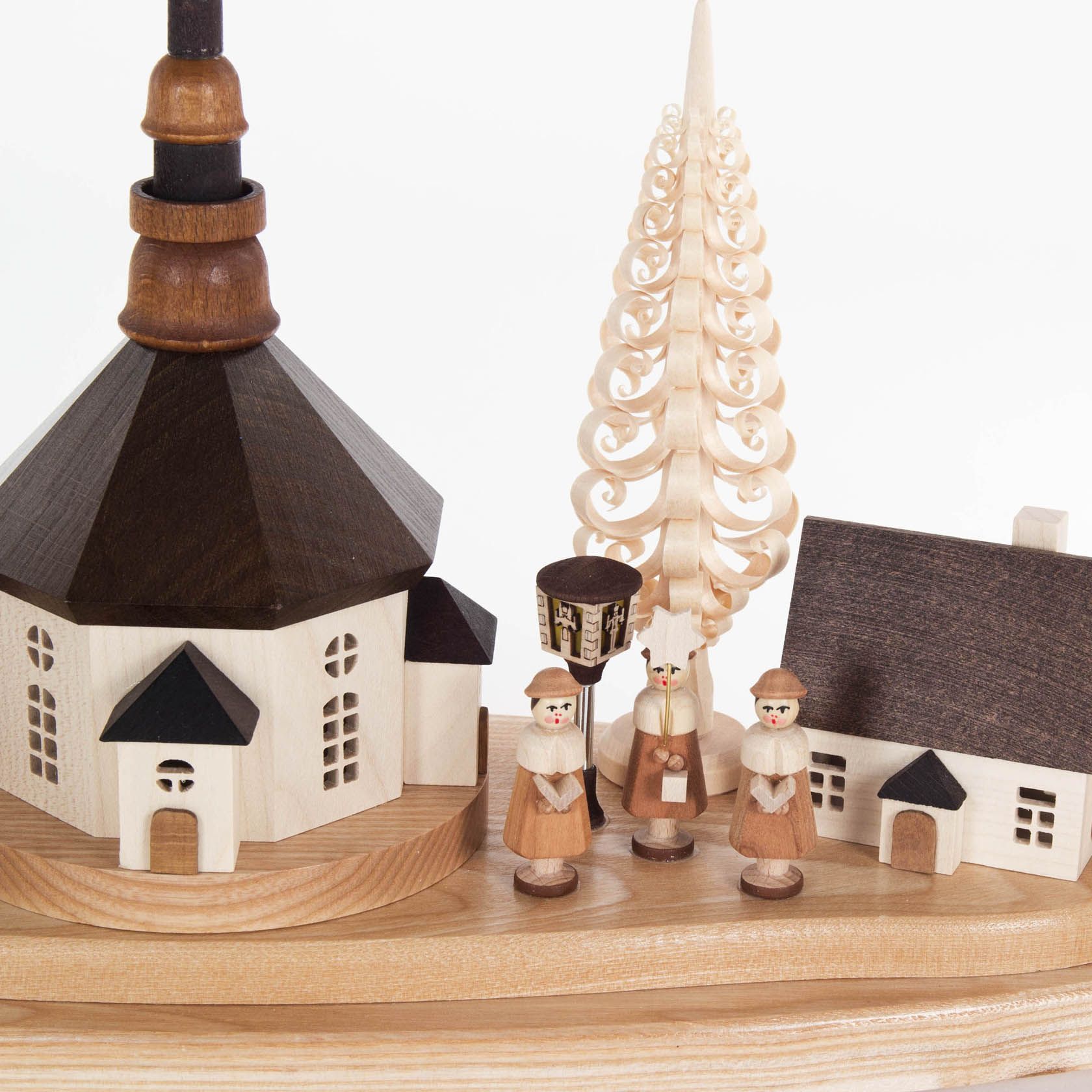 An intricate Schwibbogen showcasing a Seiffen village, with electrically lit buildings and lanterns. Three wooden figures in traditional attire stand in front.
