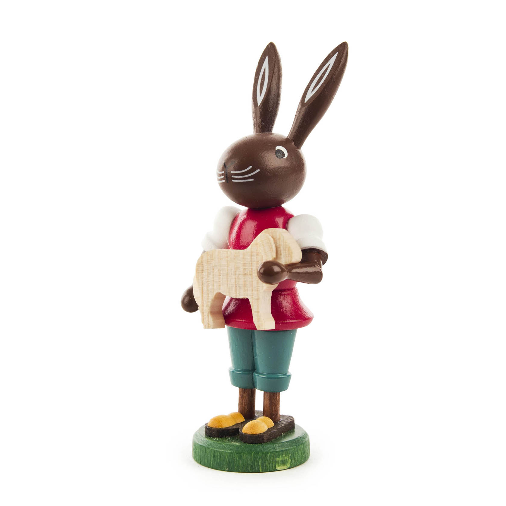 Holzfigur eines Hasen in rotem Hemd und grüner Hose, der ein kleines Schäfchen in seinen Händen hält.