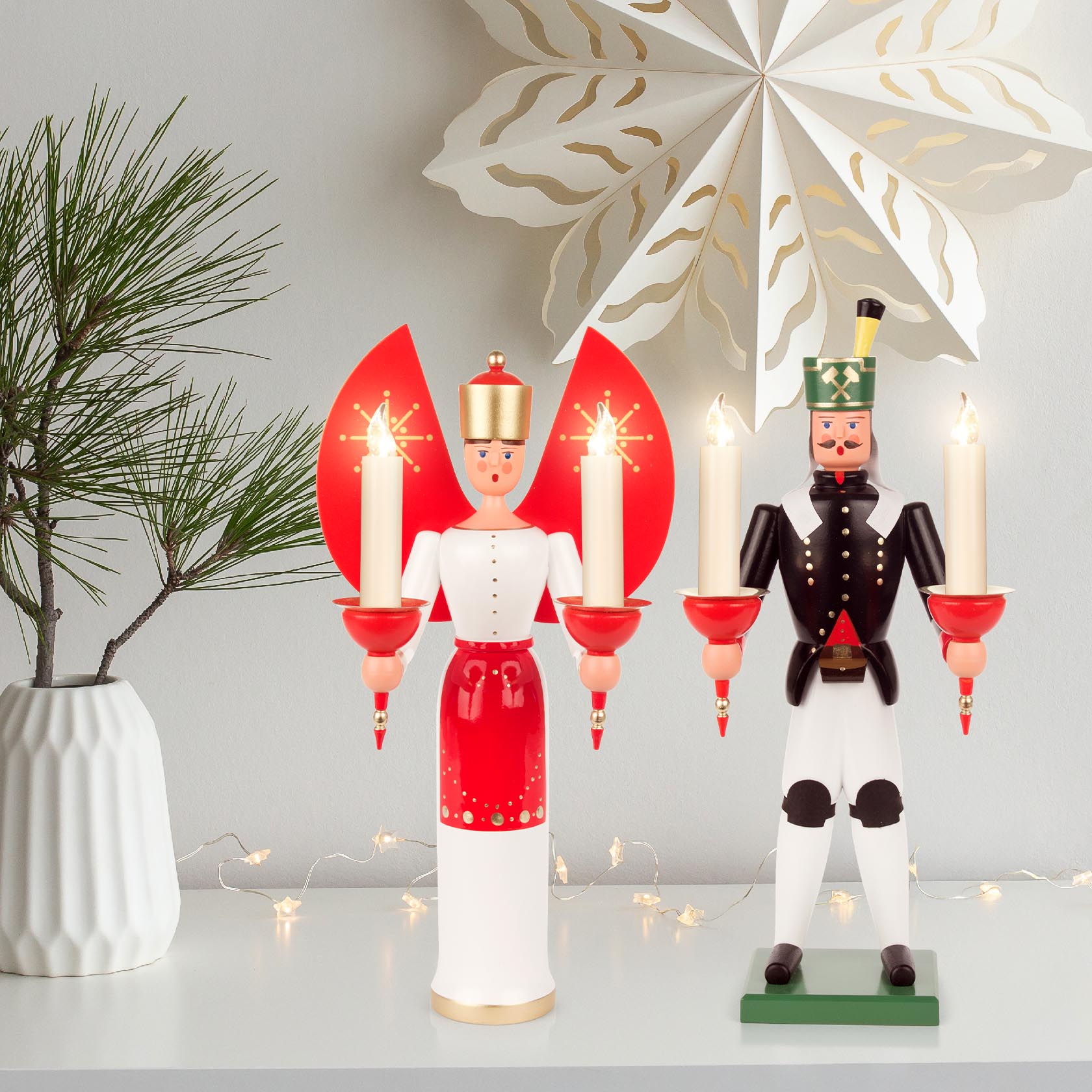 Zwei traditionelle erzgebirgische Figuren: Eine Engelsfigur in weiß-rotem Kleid mit Kerzen und ein Bergmann in Uniform, beide halten beleuchtete Kerzen.
