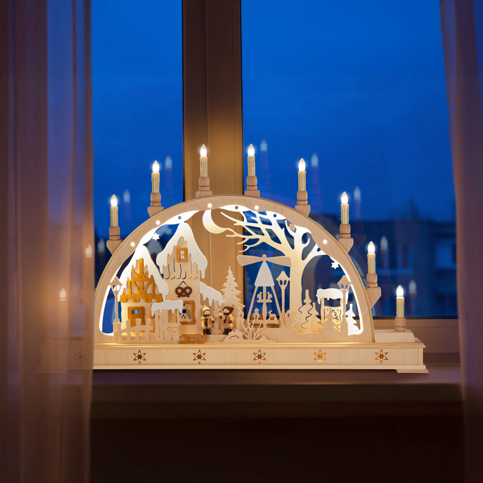 A wooden arch-shaped candle holder, or Schwibbogen, depicting an illuminated Christmas market scene with trees, houses, and figurines.