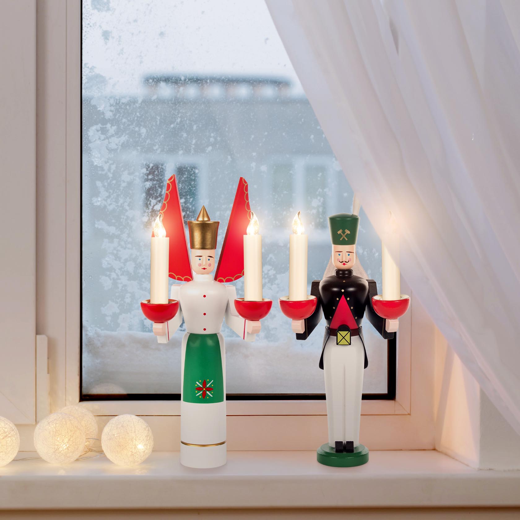 A wooden angel with a green apron and red wings, and a wooden miner with a green hat and black uniform, each holding candle holders in their hands.