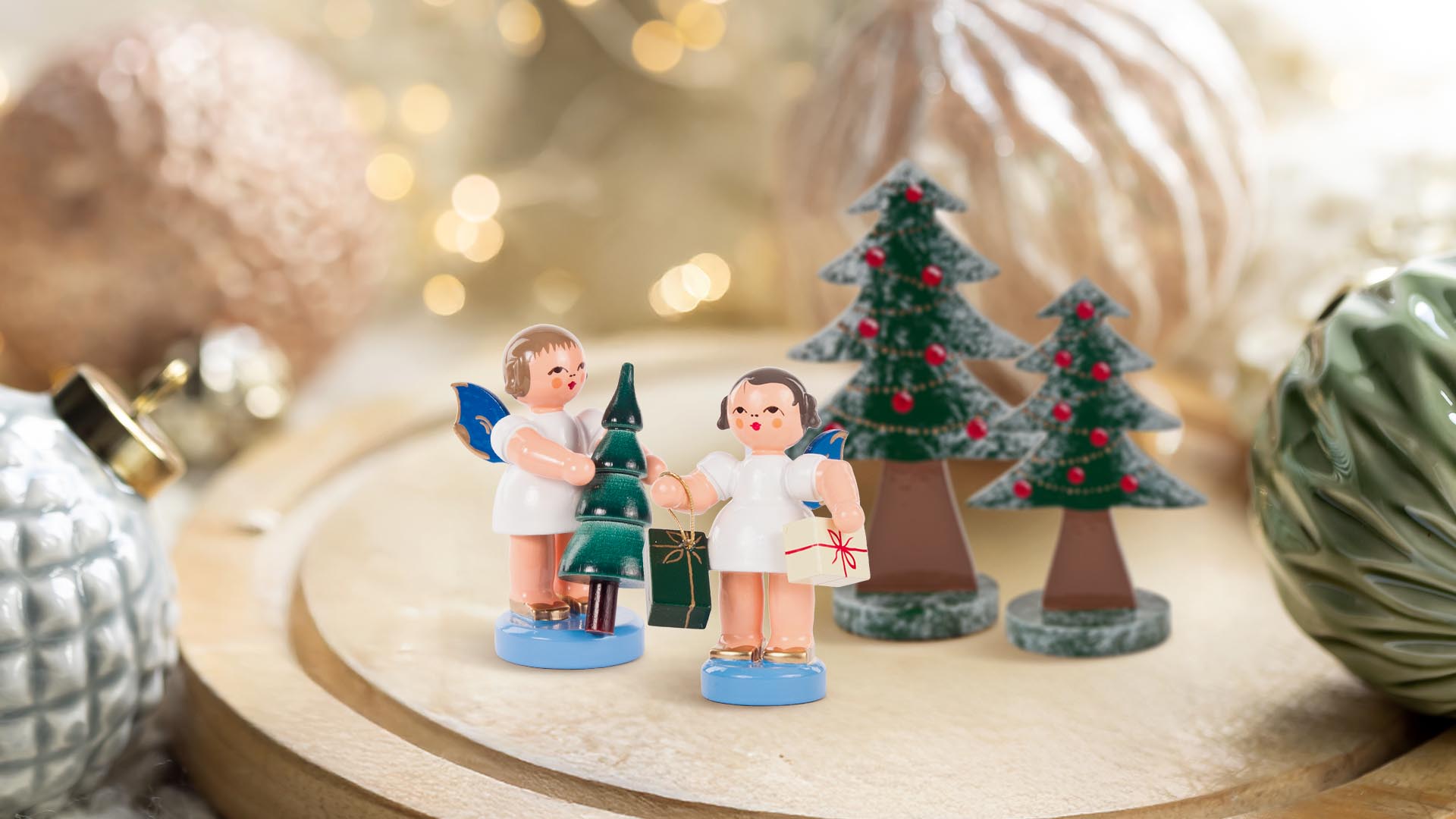 Engelpaar mit Weihnachtsbaum und Geschenken und zwei Bäumchen