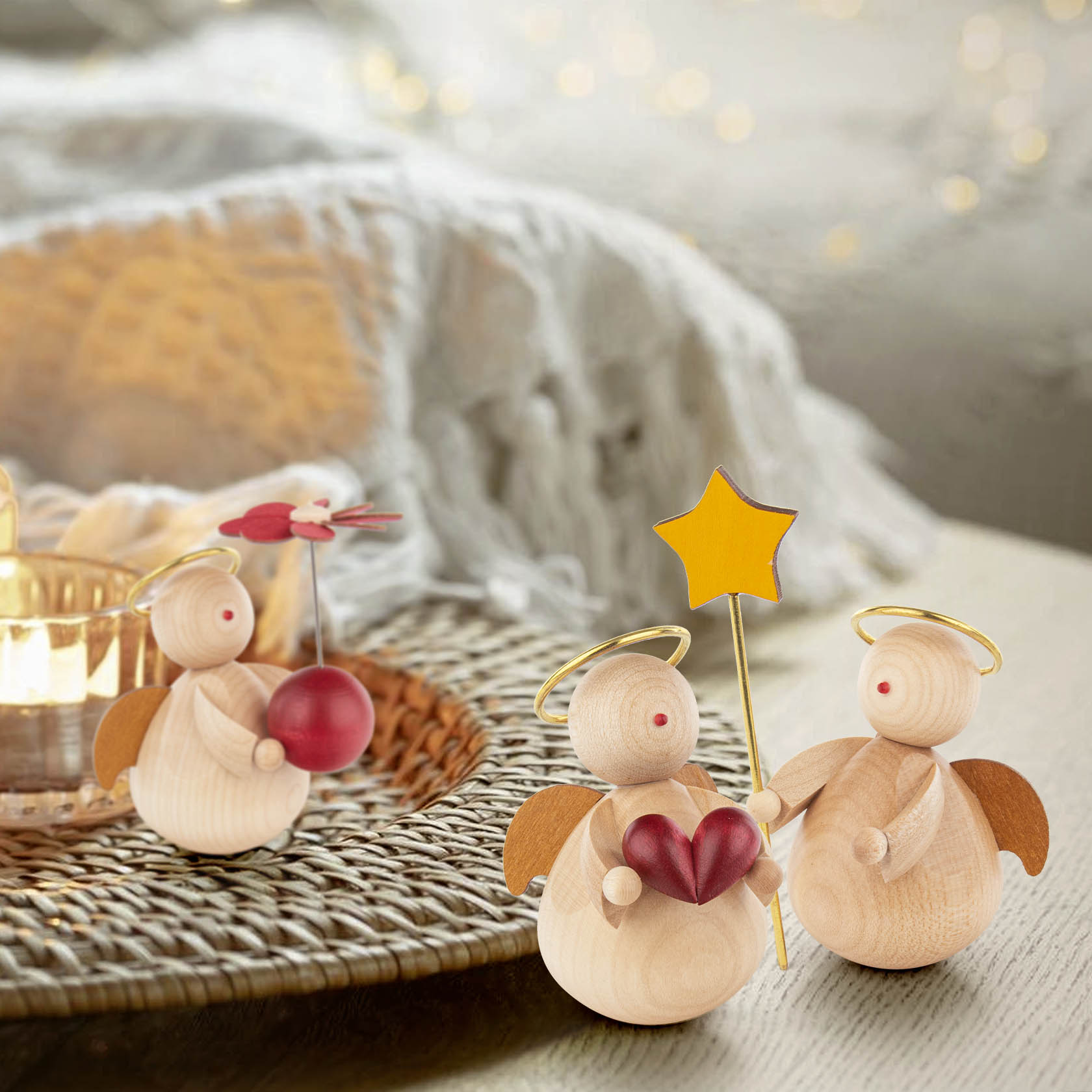 Two small wooden angel figurines with golden halos; one holds a yellow star, the other a red heart. A third angel holds a red ball nearby.