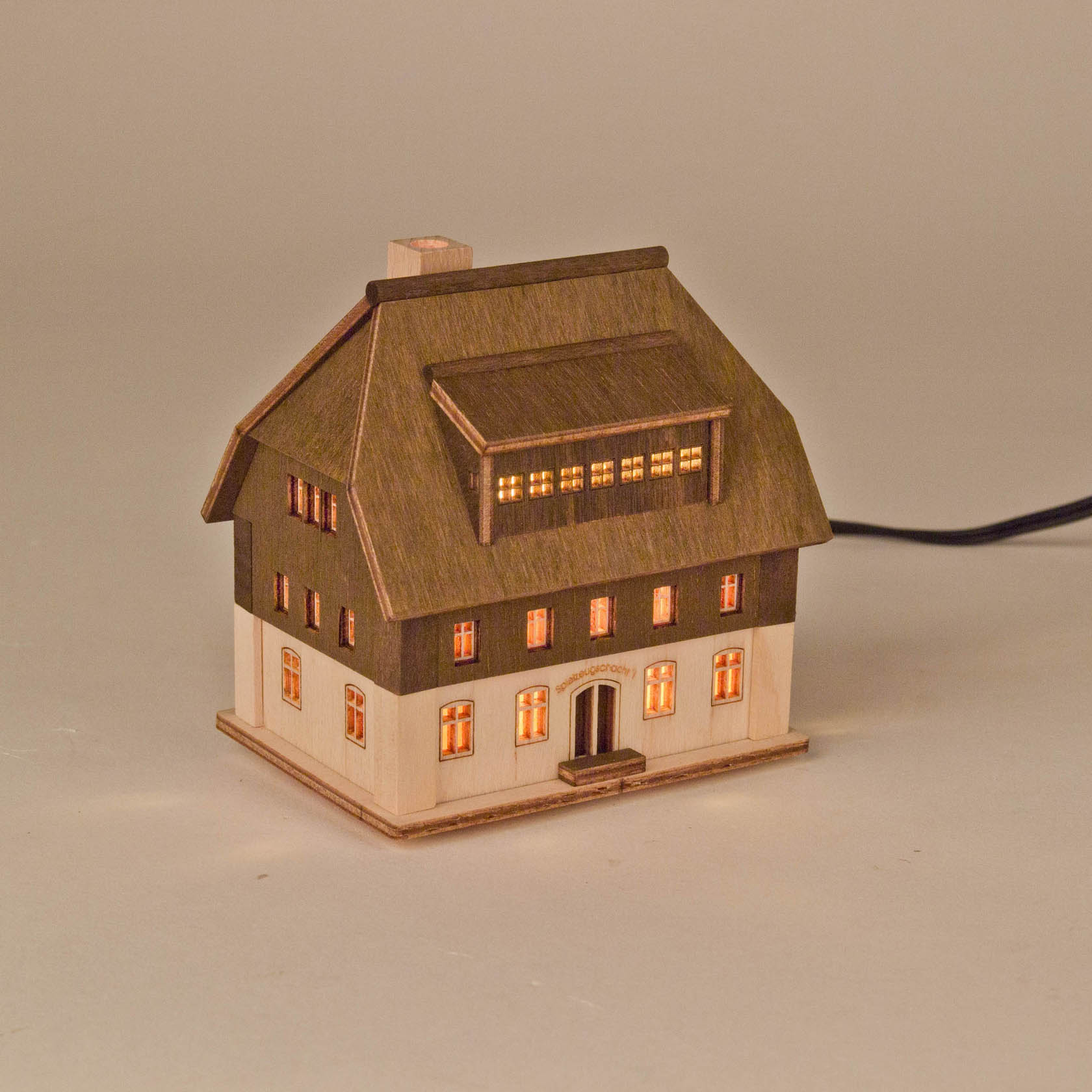 Ein beleuchtetes, miniatur Holzhaus mit mehreren Fenstern und einem Eingang, das wie ein traditionelles deutsches Haus aussieht.