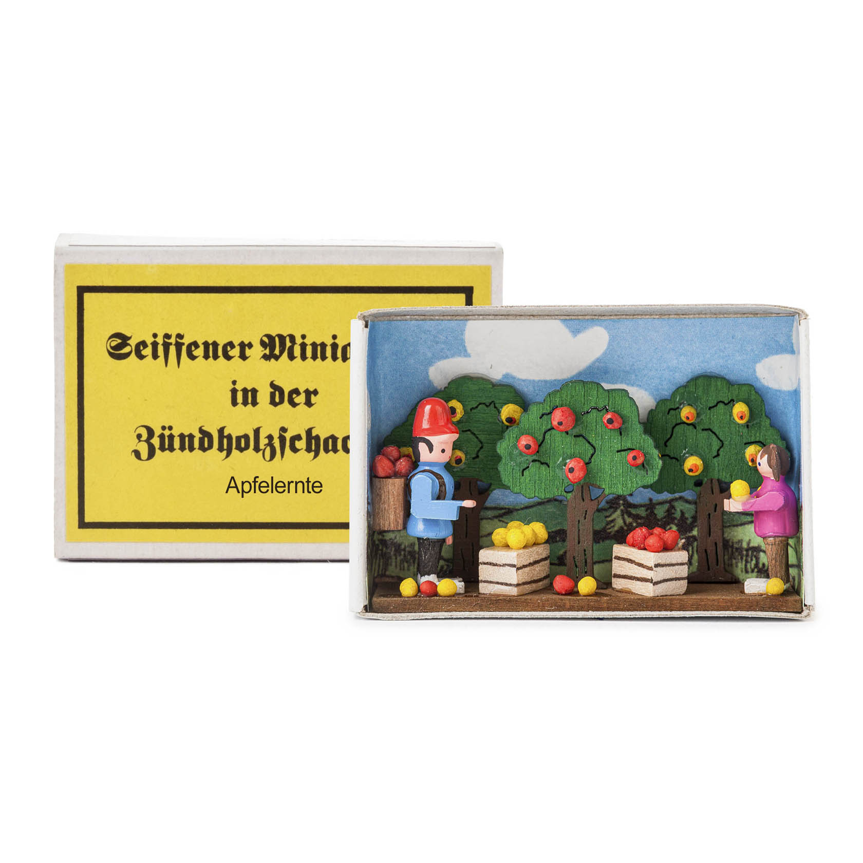 A matchbox diorama featuring two wooden figures harvesting apples from trees, with apple crates at their feet. The box is labeled 'Seiffener Miniaturen in der Zündholzschachtel Apfelernte'. im Dregeno Online Shop günstig kaufen