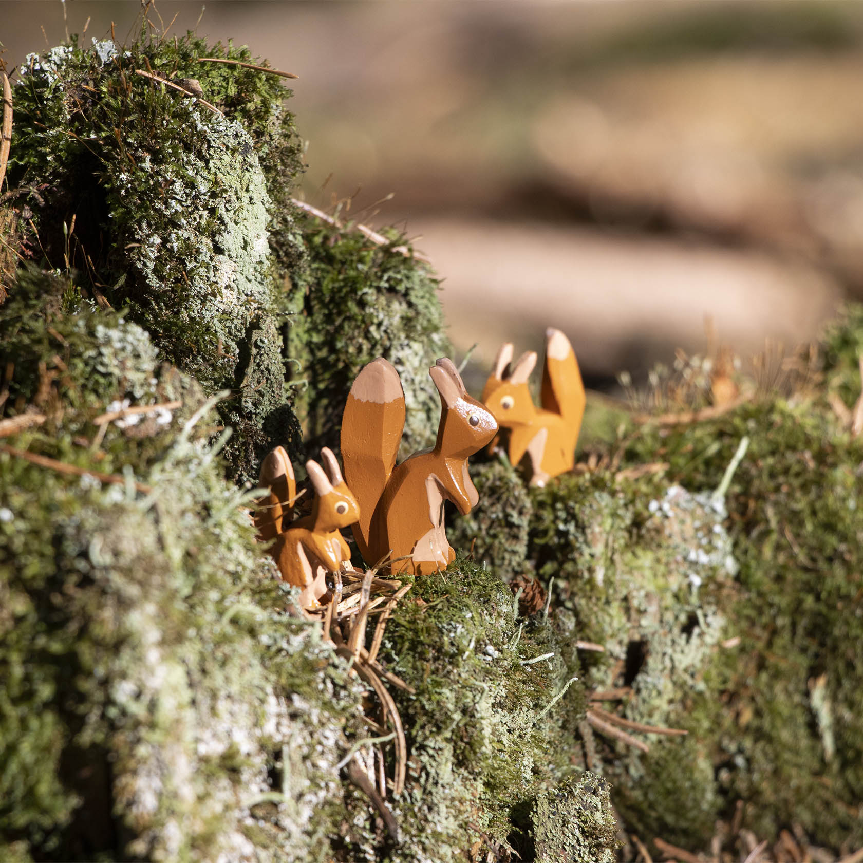 Three carved wooden squirrels with bushy tails are standing on a moss-covered rock.