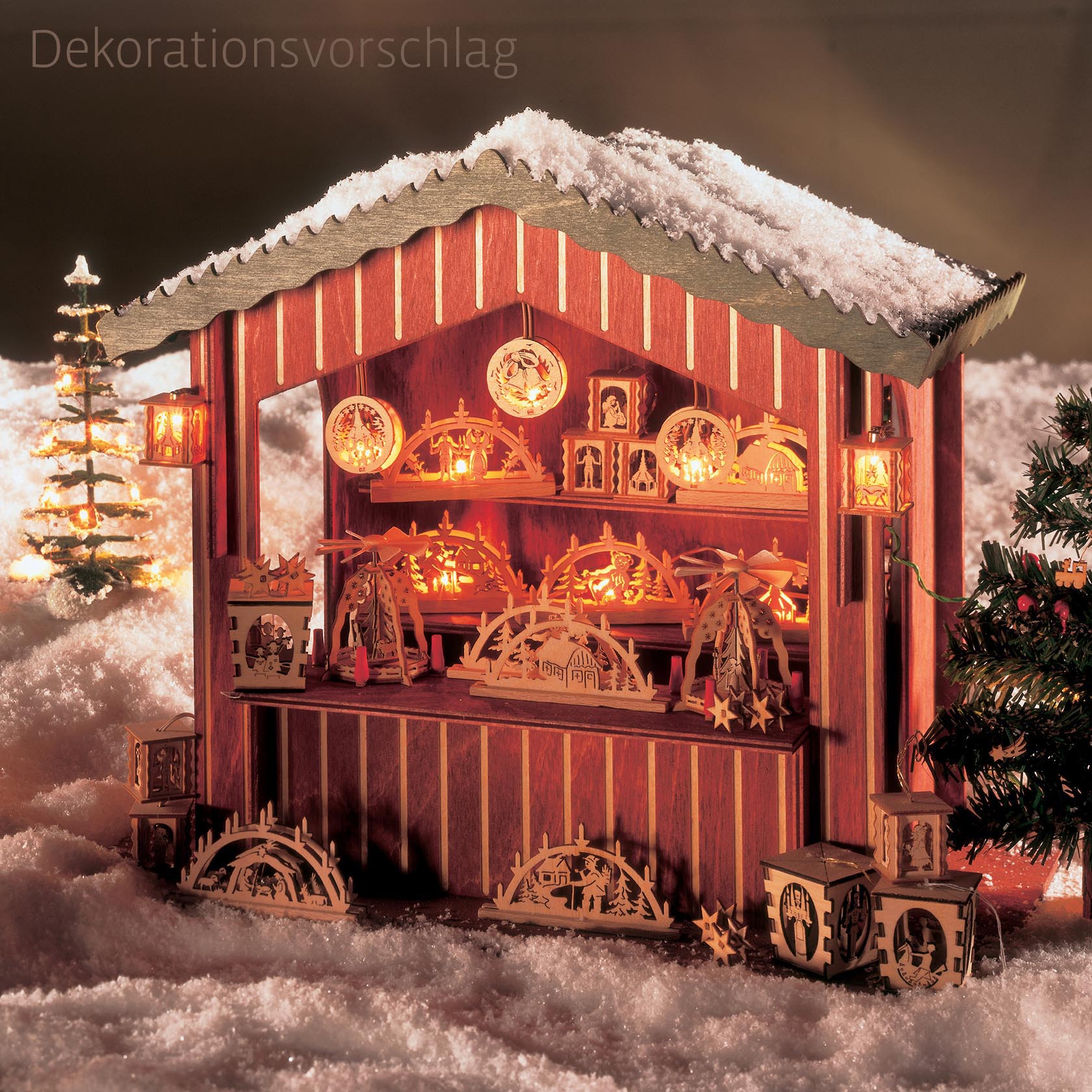 Wooden Christmas market stall model, illuminated with electric lights, showing detailed carvings and snowy decoration.