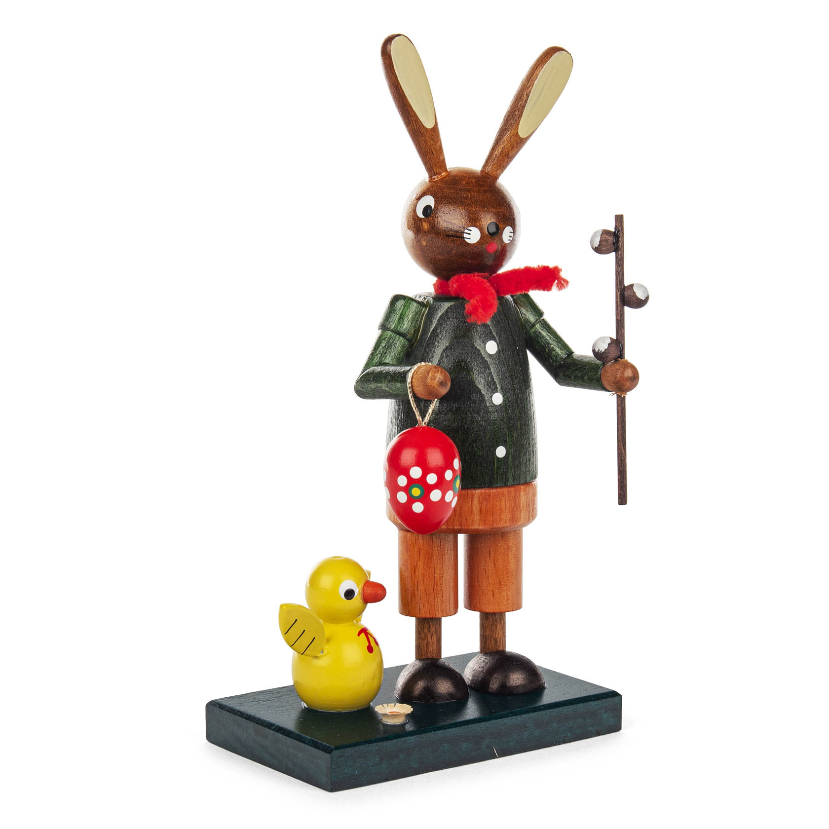 Holzfigur eines Osterhasen in grüner Kleidung mit rotem Schal, hält einen Ast und ein buntes Osterei. Neben ihm steht ein gelbes Küken.
