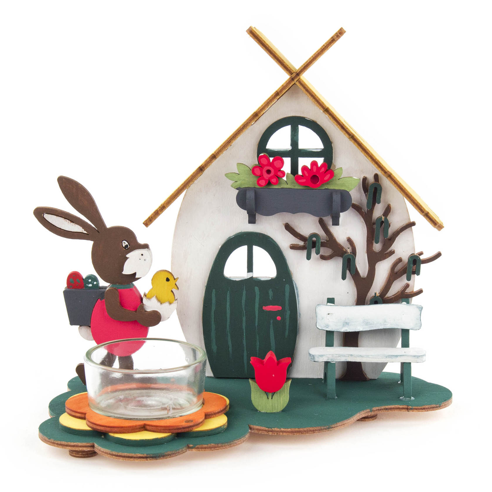 Ein dekorativer Teelichthalter in Form eines Osterhauses mit einem Hasen, der ein Küken trägt. Im Vordergrund ist ein Glas für ein Teelicht. im Dregeno Online Shop günstig kaufen