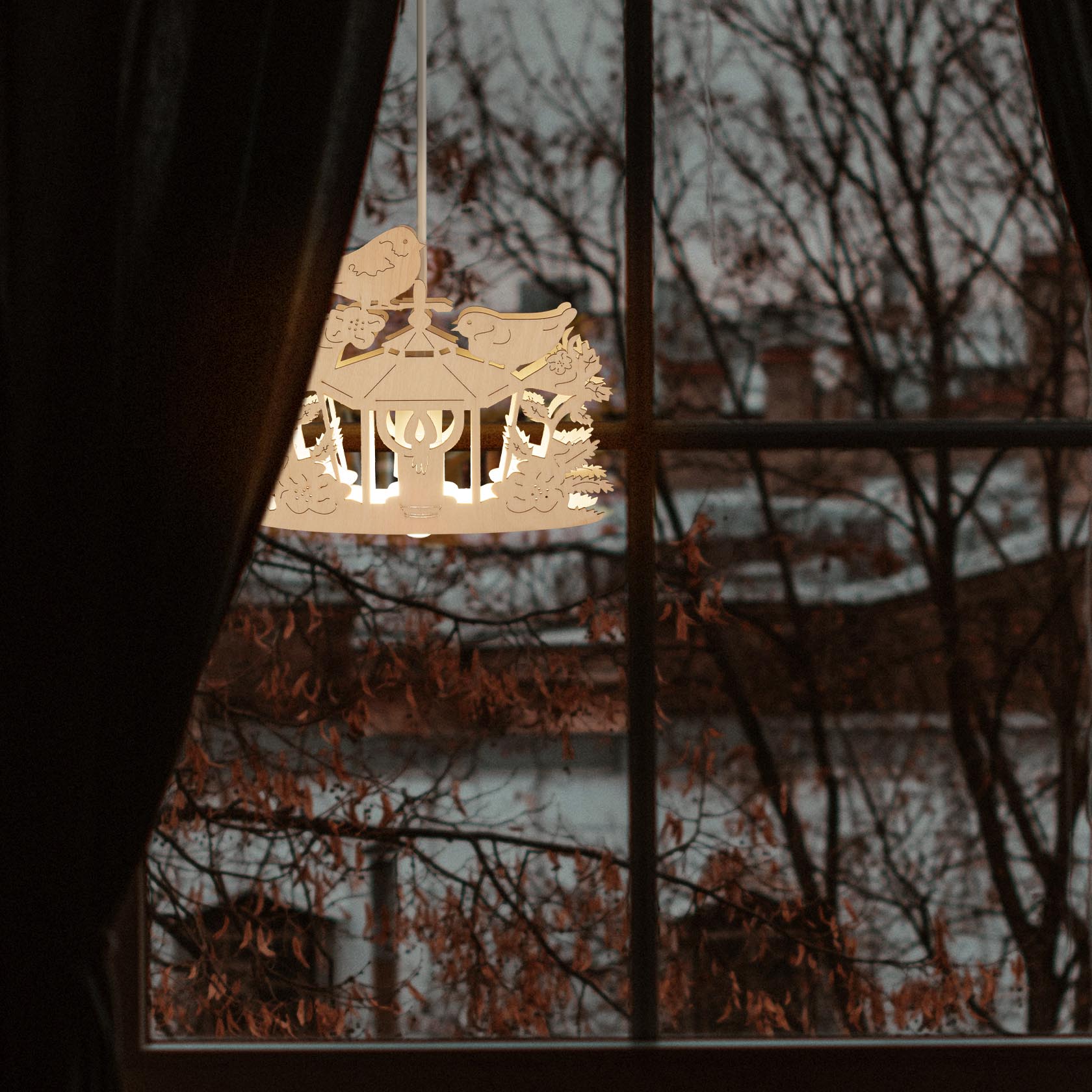 Illuminated window decoration showing a lantern with birds, hanging in front of a window with tree silhouettes visible outside.