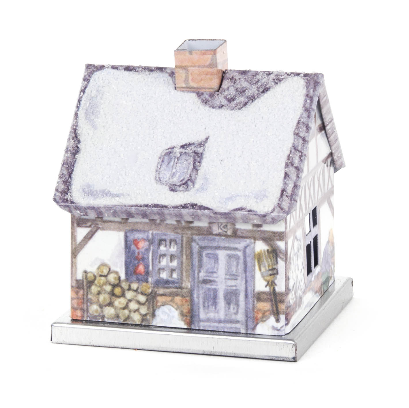 A small, metal incense house shaped like a winter-themed cottage, featuring snow-covered roof, chimney, stacked firewood, and a broom outside.