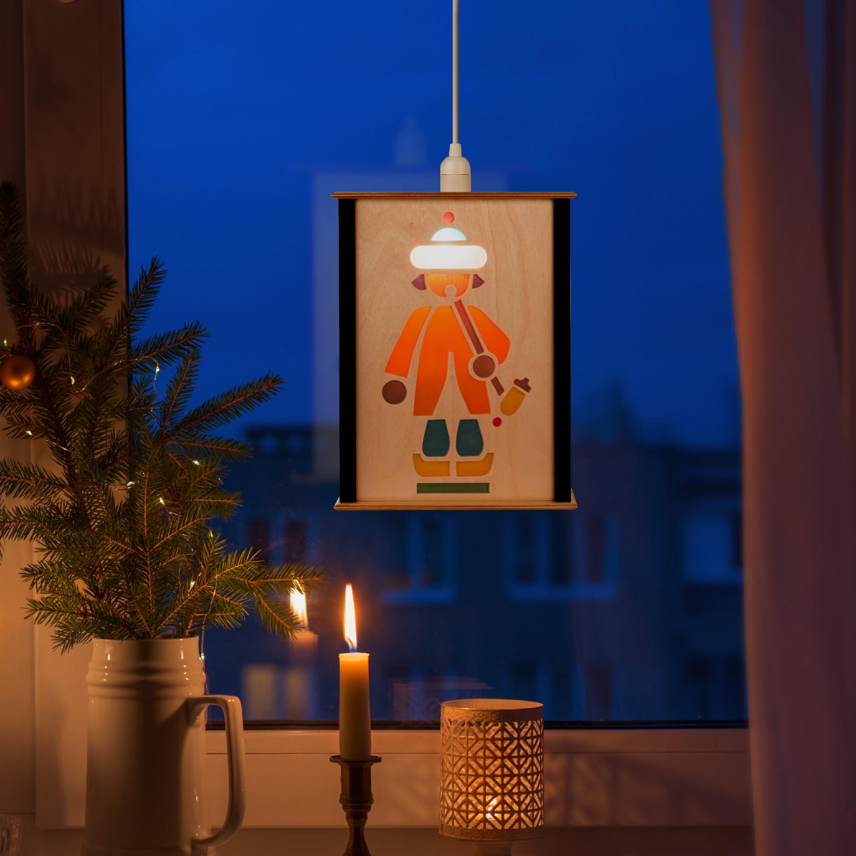 Fensterlaterne mit kindlichem Reiterlein-Motiv, beleuchtet, neben einem beleuchteten Weihnachtsbaum und einer brennenden Kerze.