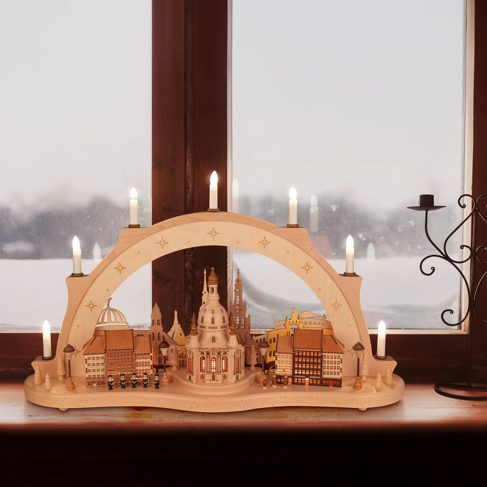 A wooden candle arch sculpture (Schwibbogen) depicting the Dresden Frauenkirche illuminated with electric lights. It is placed on a window sill.