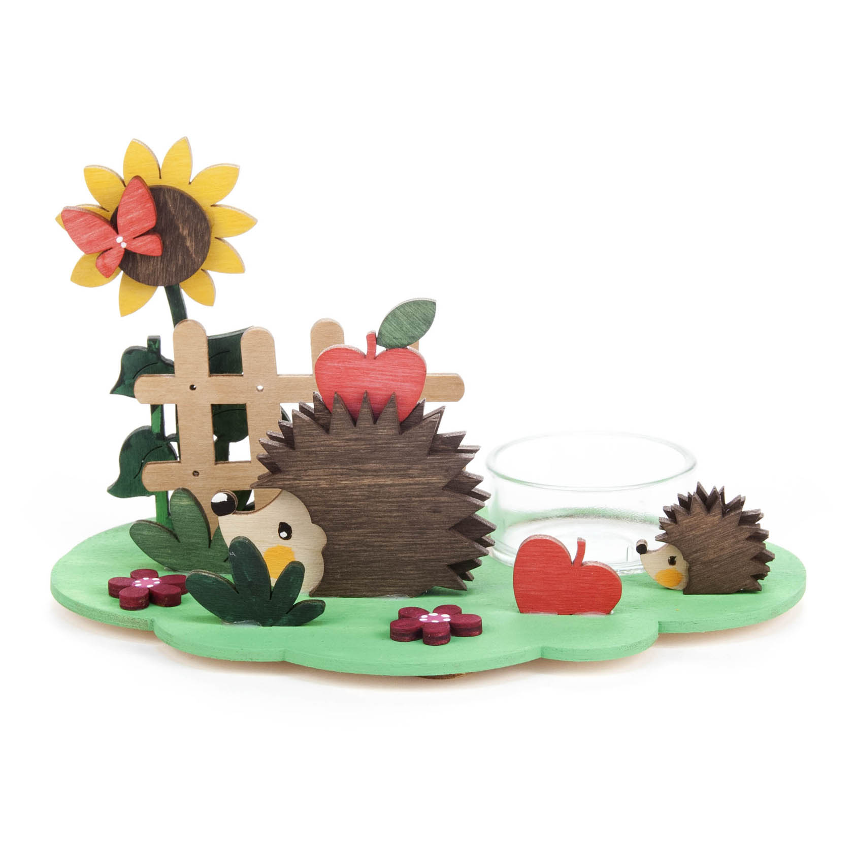 Teelichthalter im Herbstdesign mit zwei Igeln, einem Glas für das Teelicht, einer großen Sonnenblume, Apfeldeko und kleinen Blumen auf einer grünen Basis.