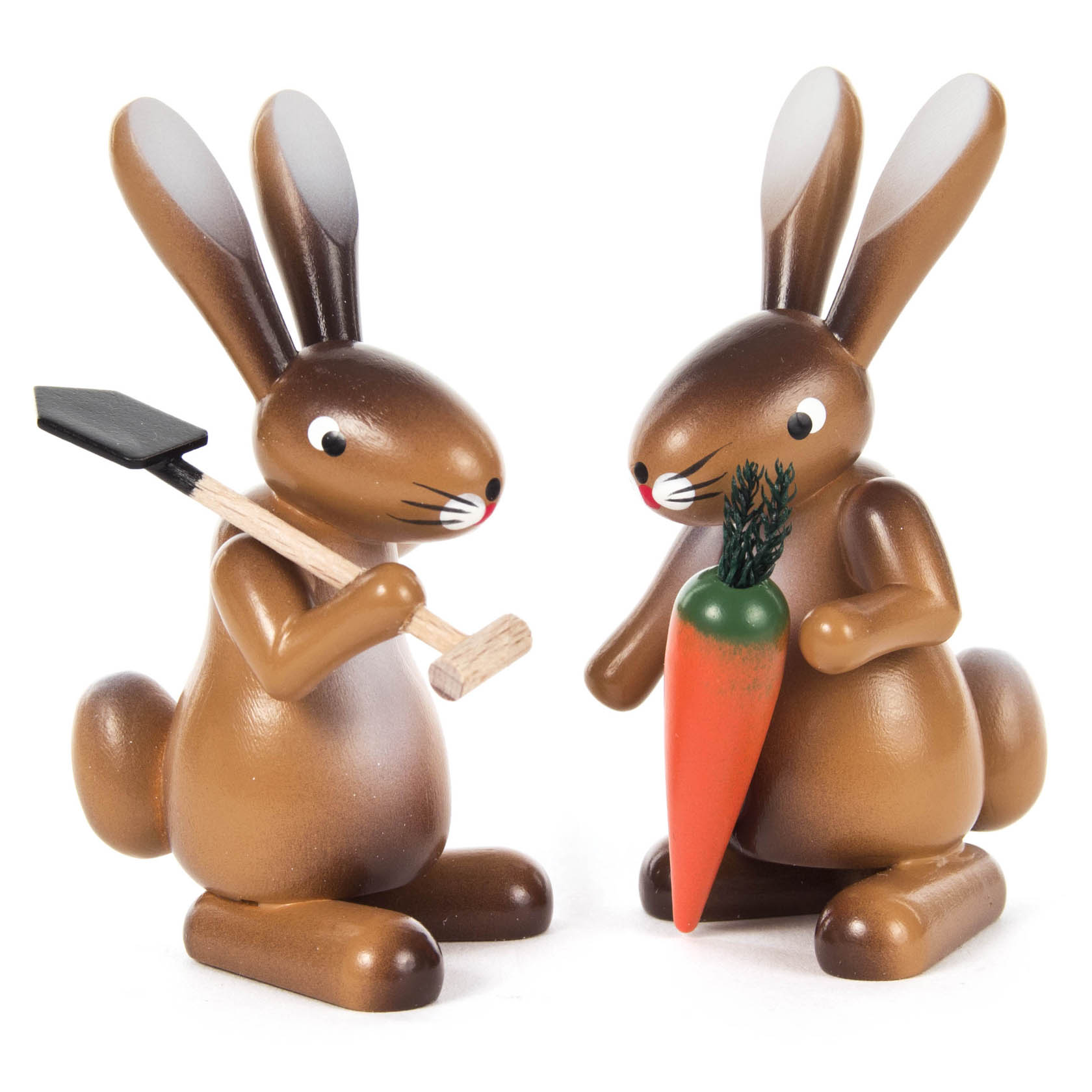 Two wooden rabbit figurines, one holding a shovel and the other holding a large carrot, both looking at each other with a friendly expression.