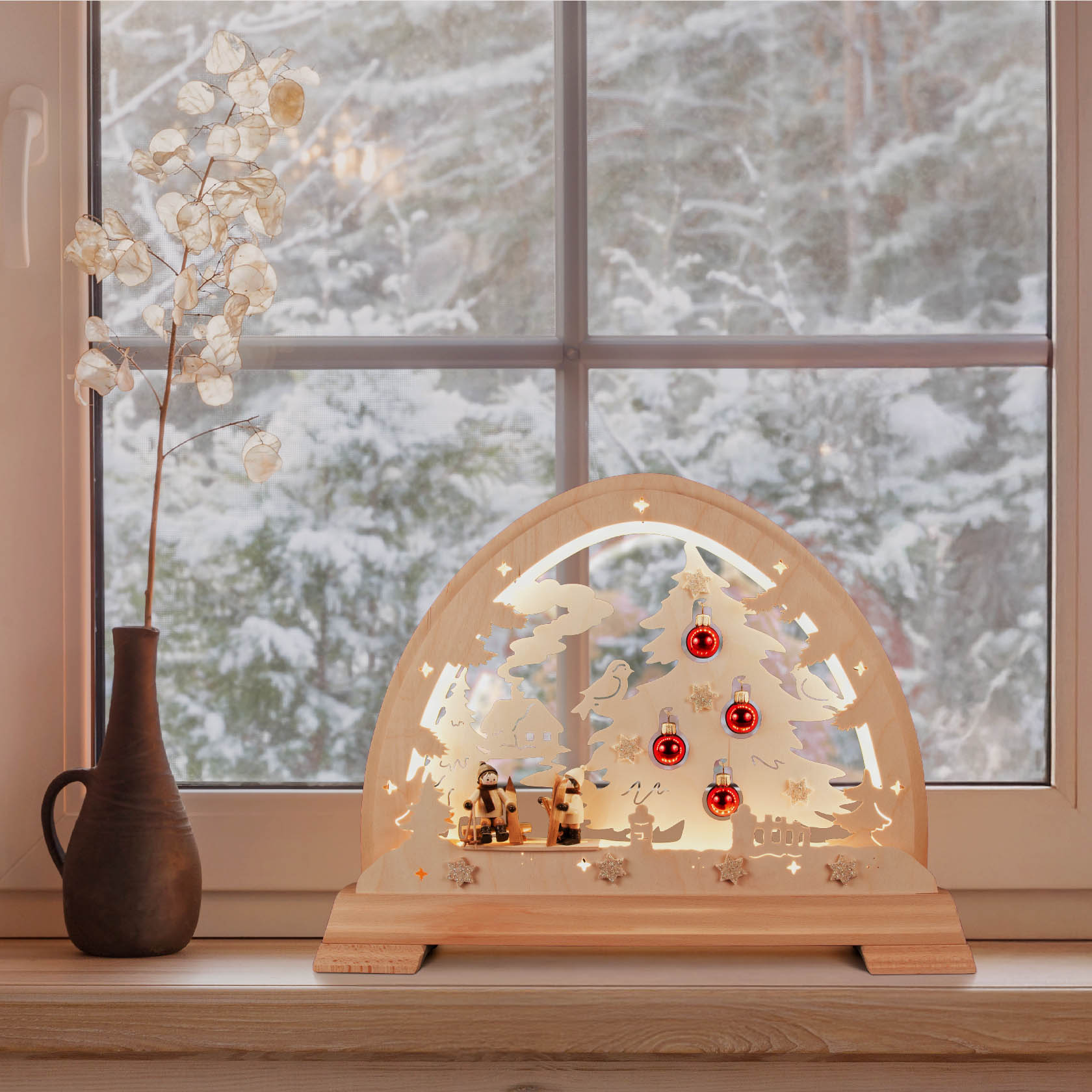 Wooden arch with LED lights featuring a skier, Christmas tree with red ornaments, and a small village scene, placed on a window sill.