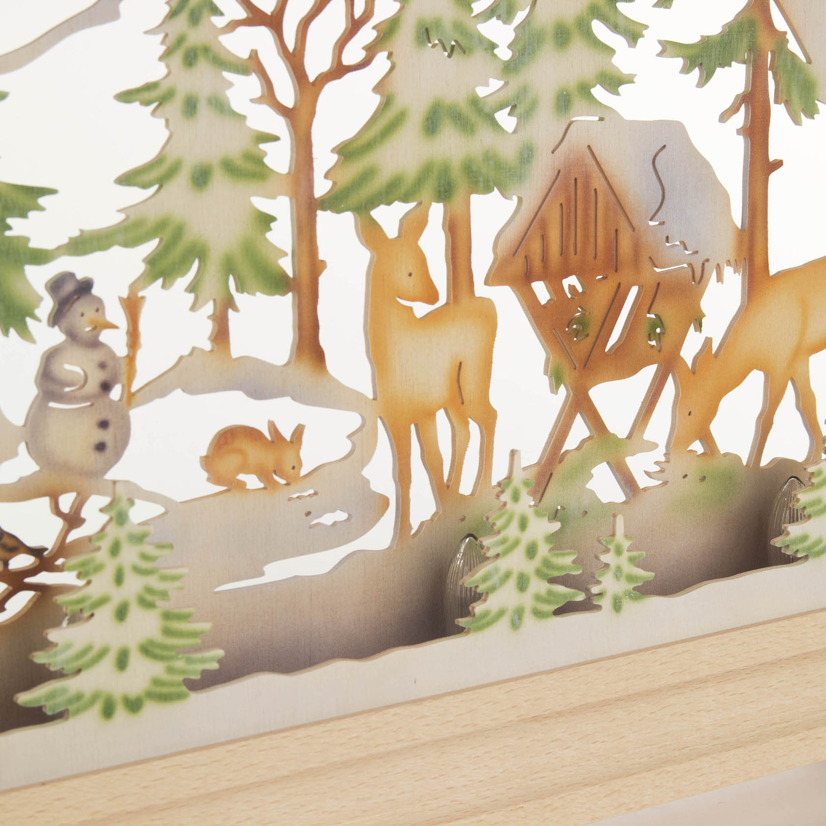 Ein farbig beleuchteter Schwibbogen aus Holz zeigt ein Forsthausszenario mit Rehen, einem Schneemann und einem Hasen zwischen Tannenbäumen.