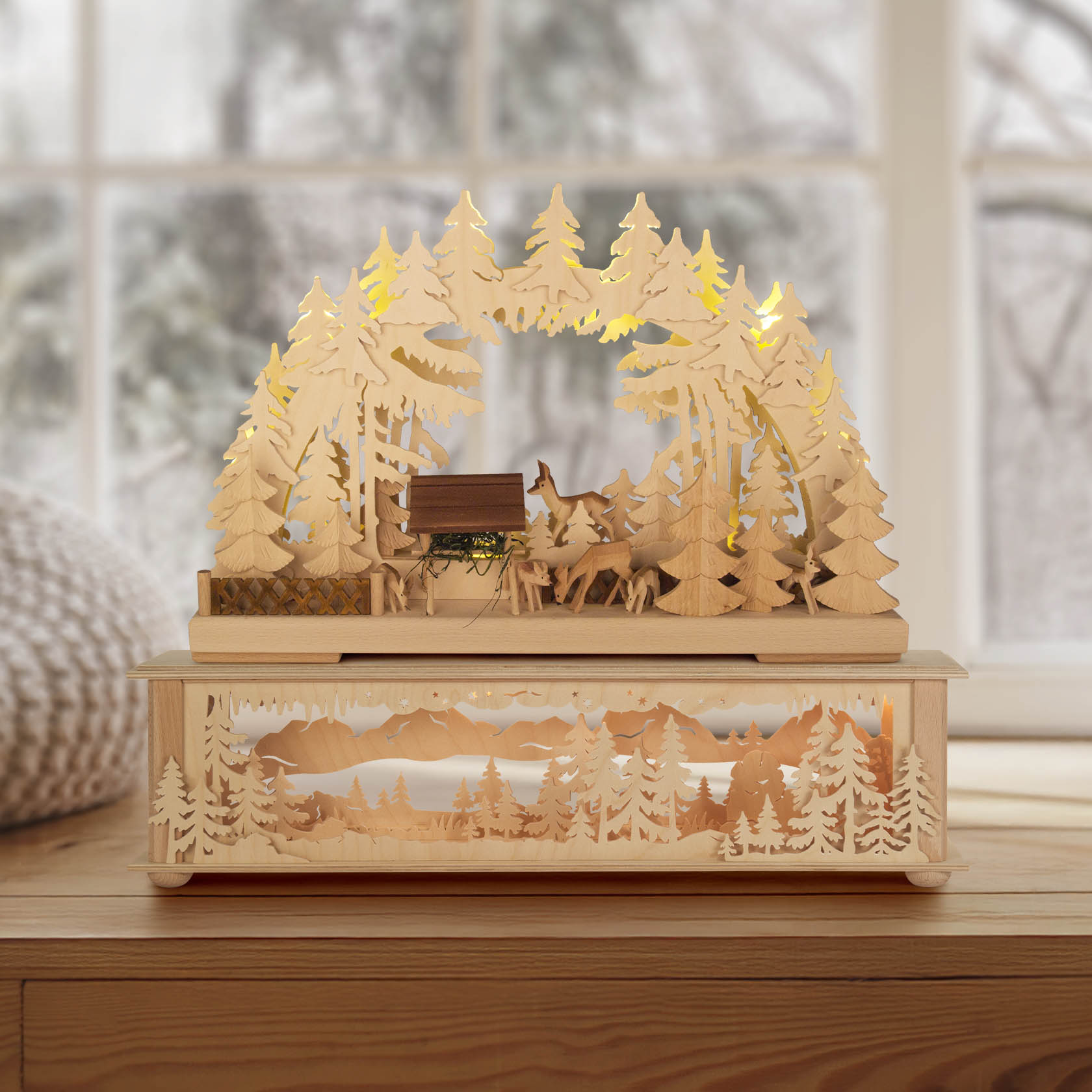 Ein kleiner Schwibbogen mit Titel 'Wildfütterung', zeigt eine Szene von Rehen im Wald mit Futterkrippe aus Holz, indirekt elektrisch beleuchtet.