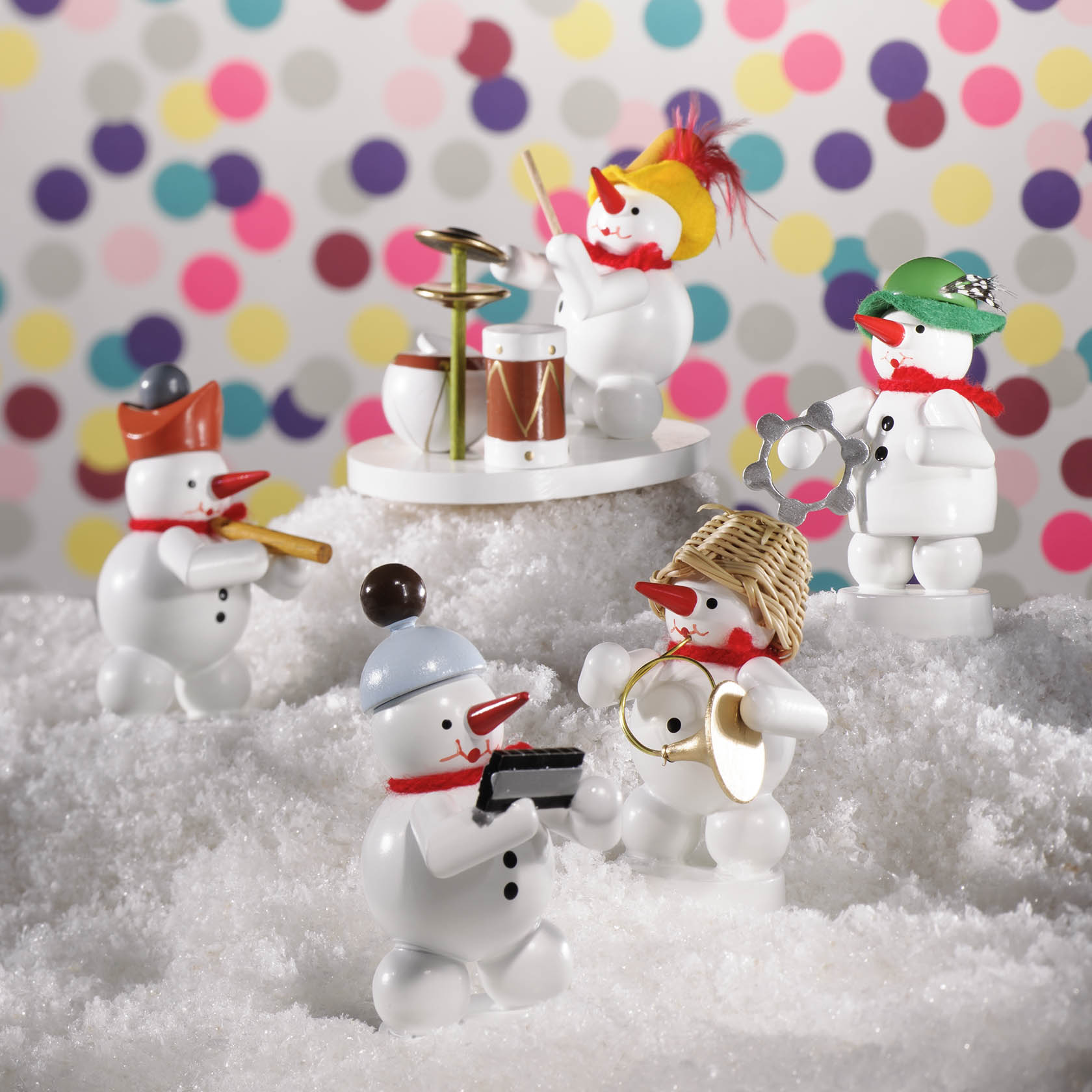A group of five snowmen figurines, each playing a different musical instrument, including a French horn. Snow covers the ground.