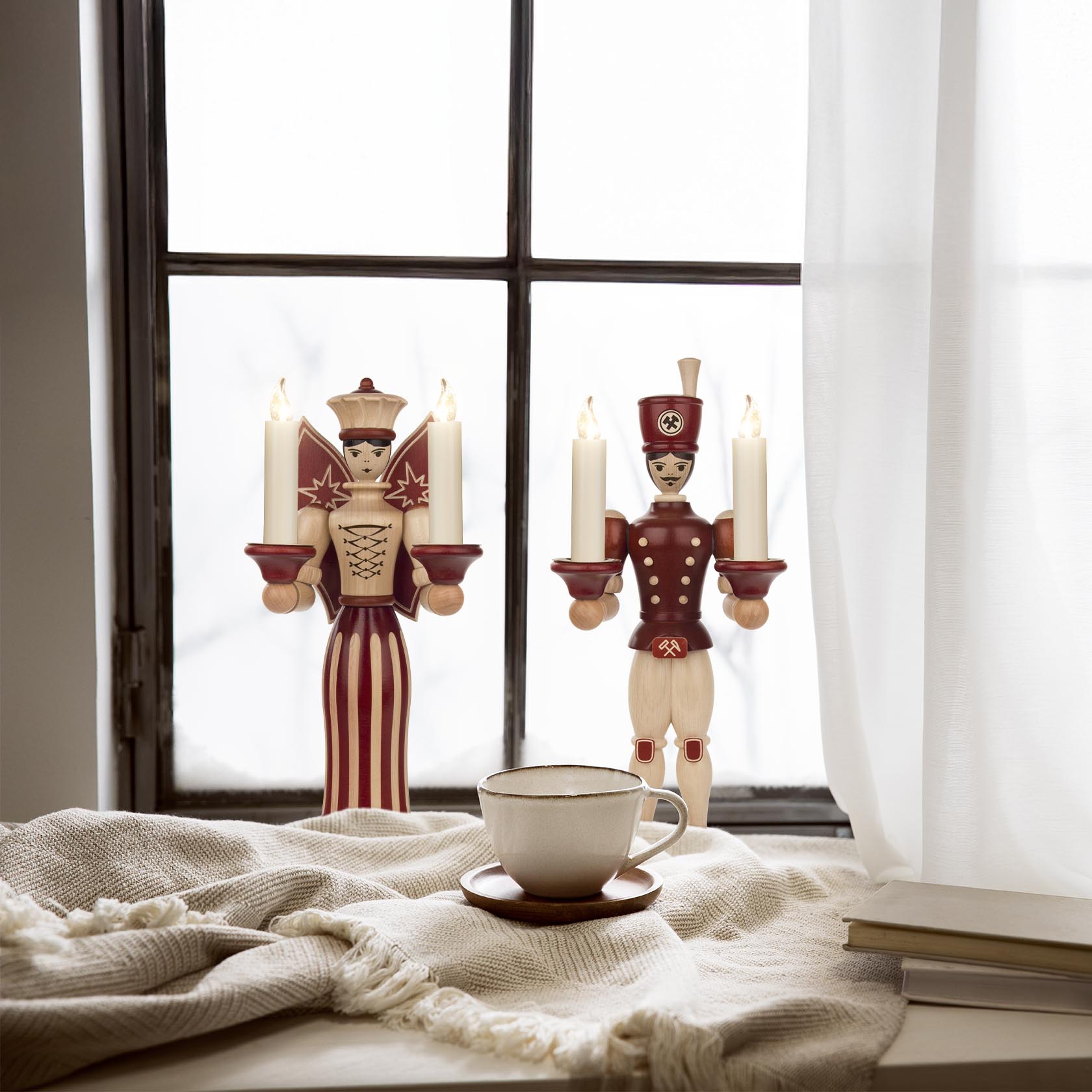 A decorative angel figure holding multiple candle holders for 14mm candles, placed on a windowsill, accompanied by a teacup on a table.