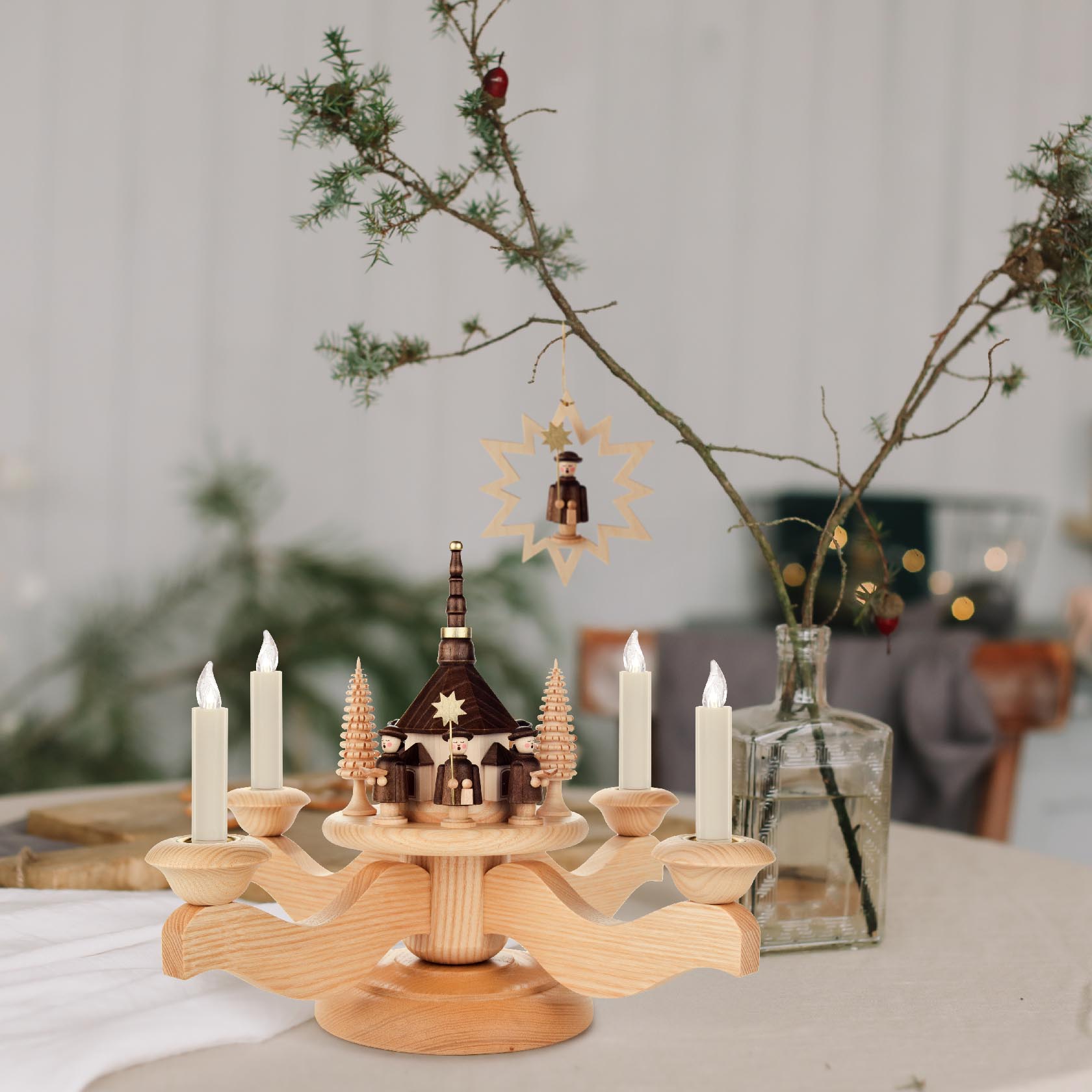 Adventsleuchter mit Seiffener Kirche in der Mitte, umgeben von vier braunen Häusern. Sechs weiße Kerzen auf dem runden, hölzernen Leuchter platziert.