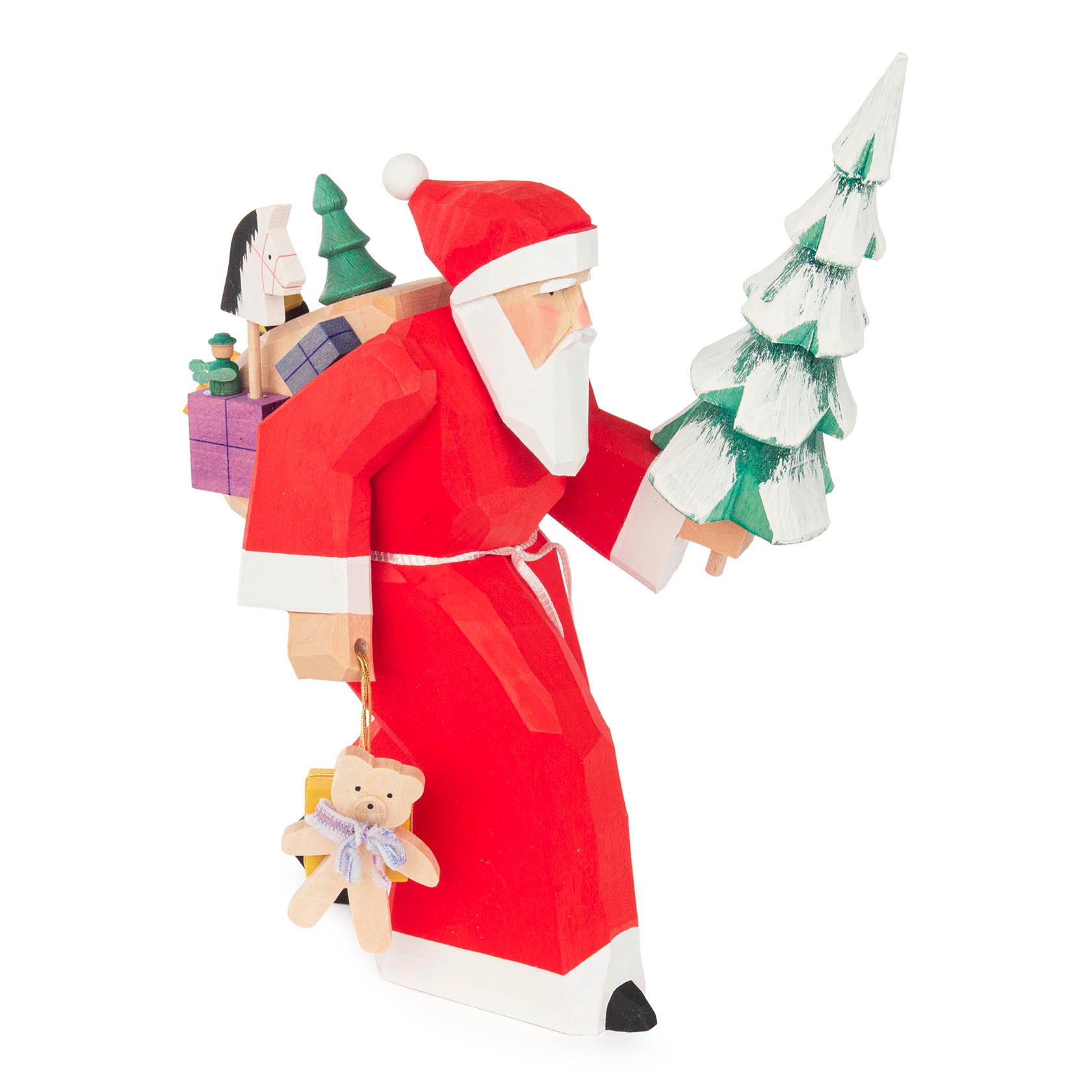 A carved wooden figure of Santa Claus in a red outfit, carrying a Christmas tree and gifts on his back, with a teddy bear attached to his arm.