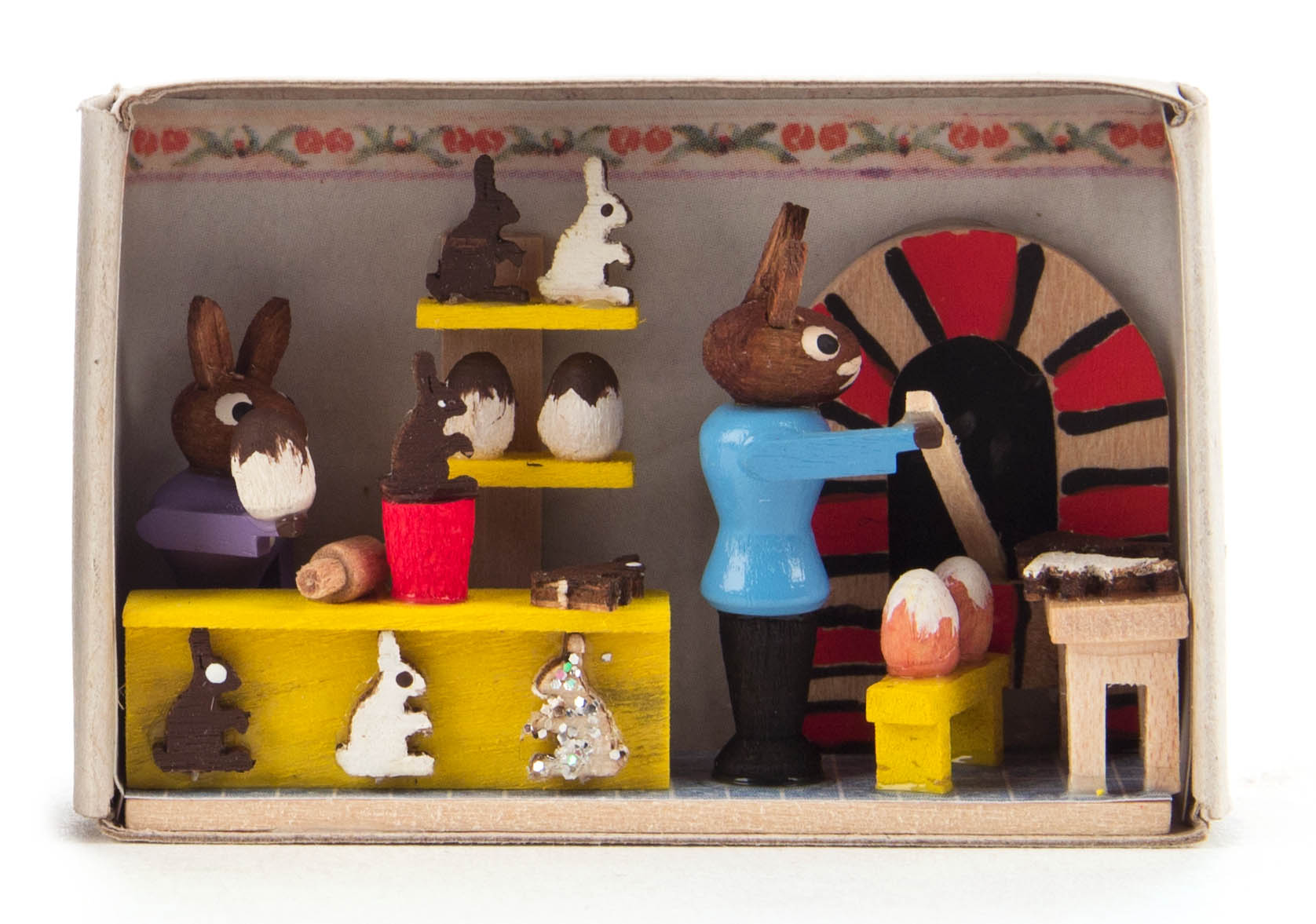 Miniature scene of a bunny bakery inside a matchbox, featuring bunnies baking and decorating Easter eggs.