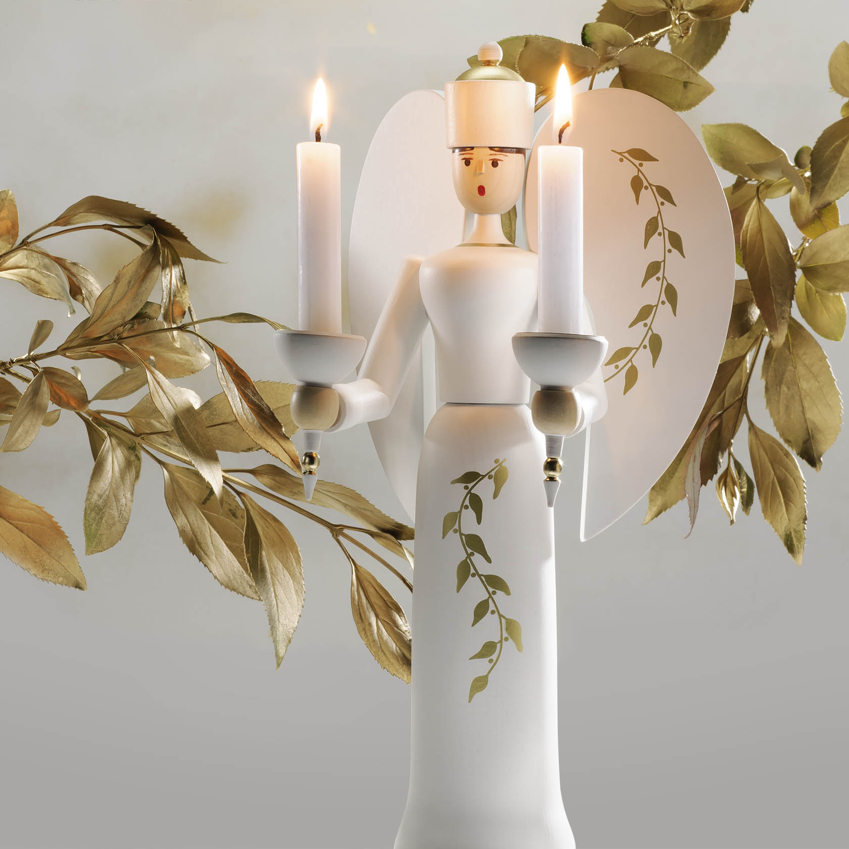 Holzengel in Weiß mit goldenen Flügeln hält zwei brennende Kerzen, hat ein florales Muster auf dem Körper. Die Kerzen sind in goldenen Haltern platziert.