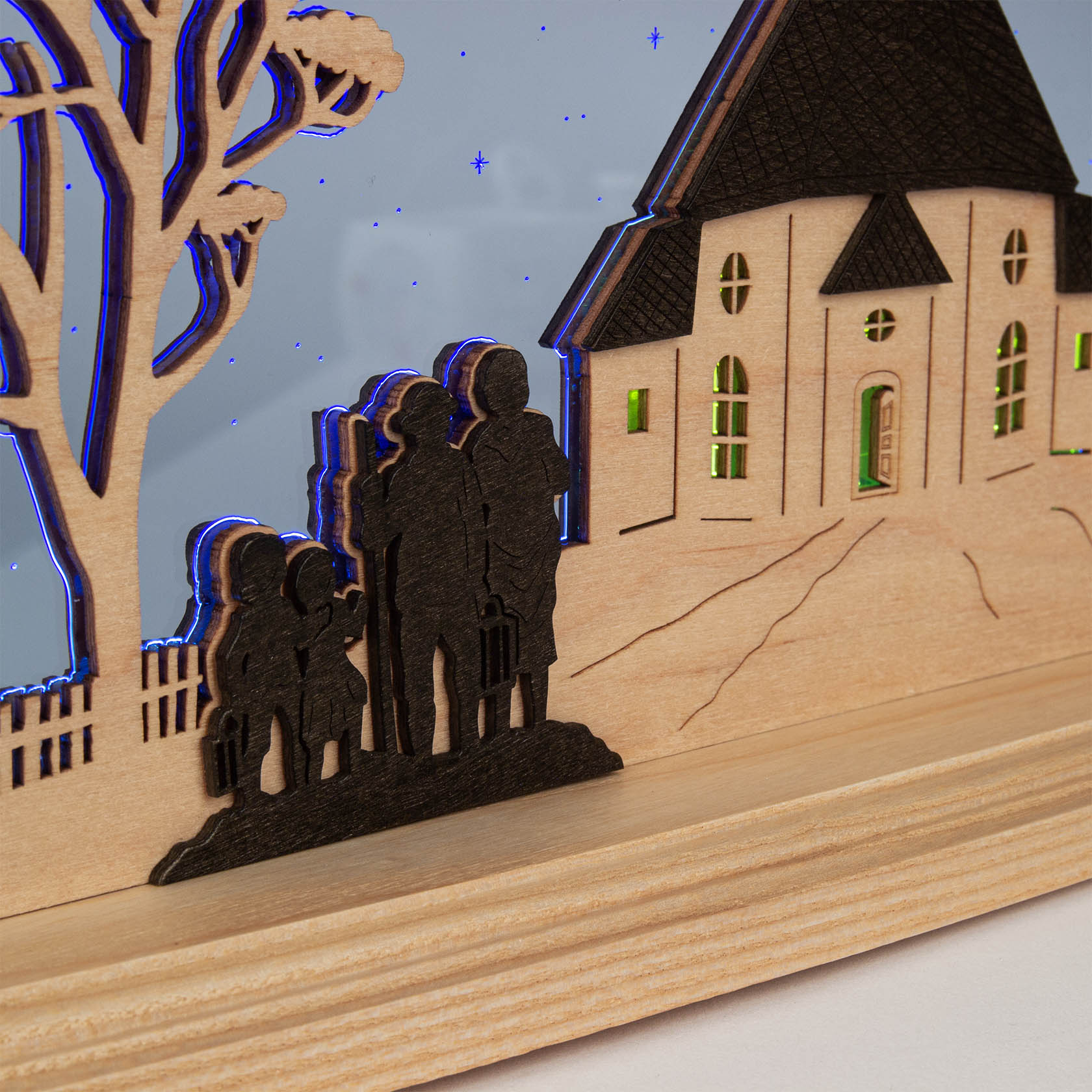 A wooden light display featuring the silhouette of the Seiffener Church with a group of five people standing to the side, two adults and three children.