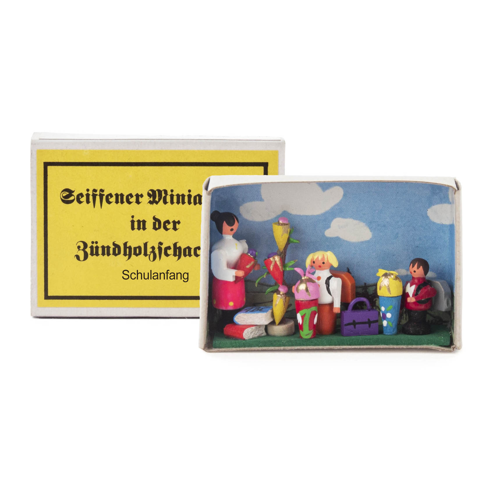 Eine geöffnete Zündholzschachtel zeigt eine Miniaturszene mit einem Lehrer und drei Kindern zur Einschulung mit einer Schultüte im Klassenzimmer. im Dregeno Online Shop günstig kaufen