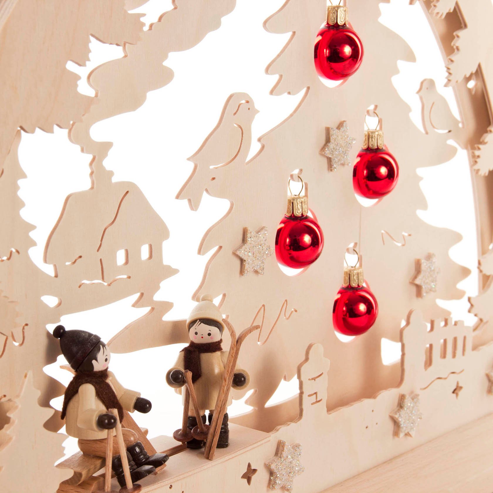 Wooden arch decoration with two skiers in warm clothing and a Christmas tree with red ornaments and LED lighting.