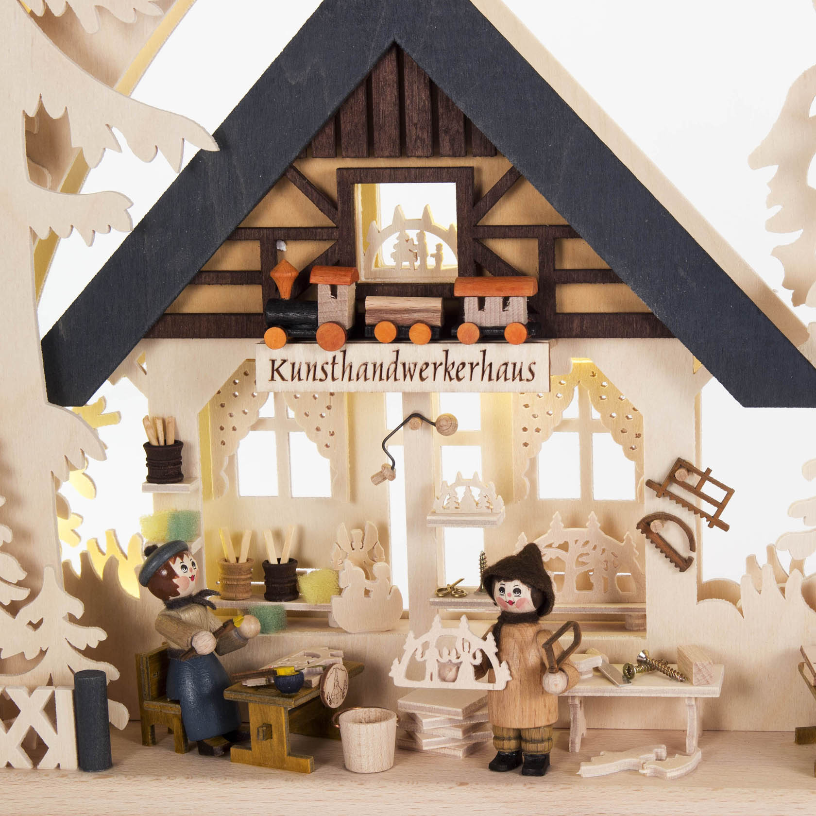 Ein Schwibbogen zeigt eine Werkstatt mit zwei Figuren, die Holzarbeiten machen. Die Werkstatt ist mit kleinen Werkzeugen ausgestattet und trägt das Schild 'Kunsthandwerkerhaus'.