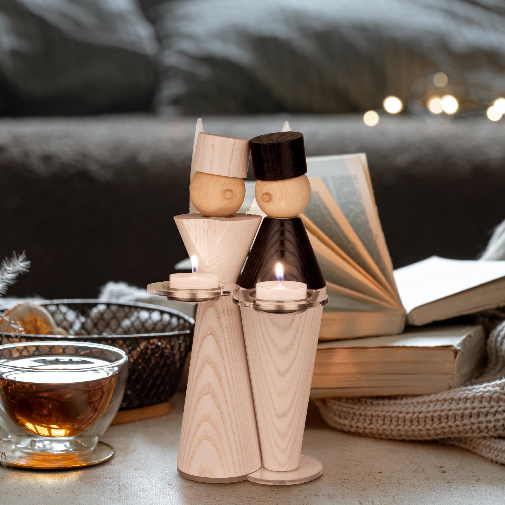 Zwei holzgeschnitzte Bergmannfiguren halten je ein Teelicht. Sie stehen nebeneinander auf einem Tisch, im Hintergrund ist eine geöffnete Buchseite sichtbar.
