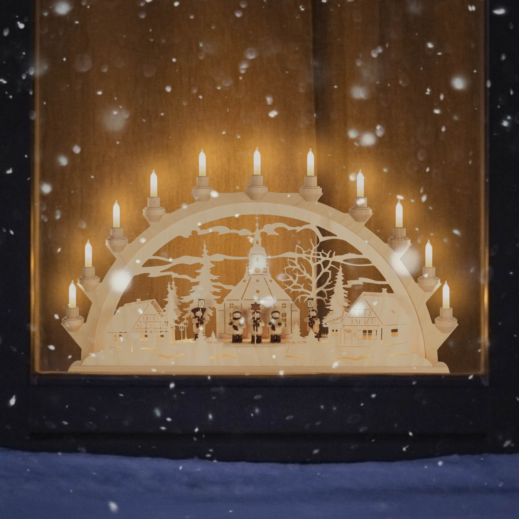 Ein Schwibbogen mit Seiffener Dorfszene und Kurrende, beleuchtet mit elf kleinen elektrischen Kerzen, auf einem Fensterbrett.