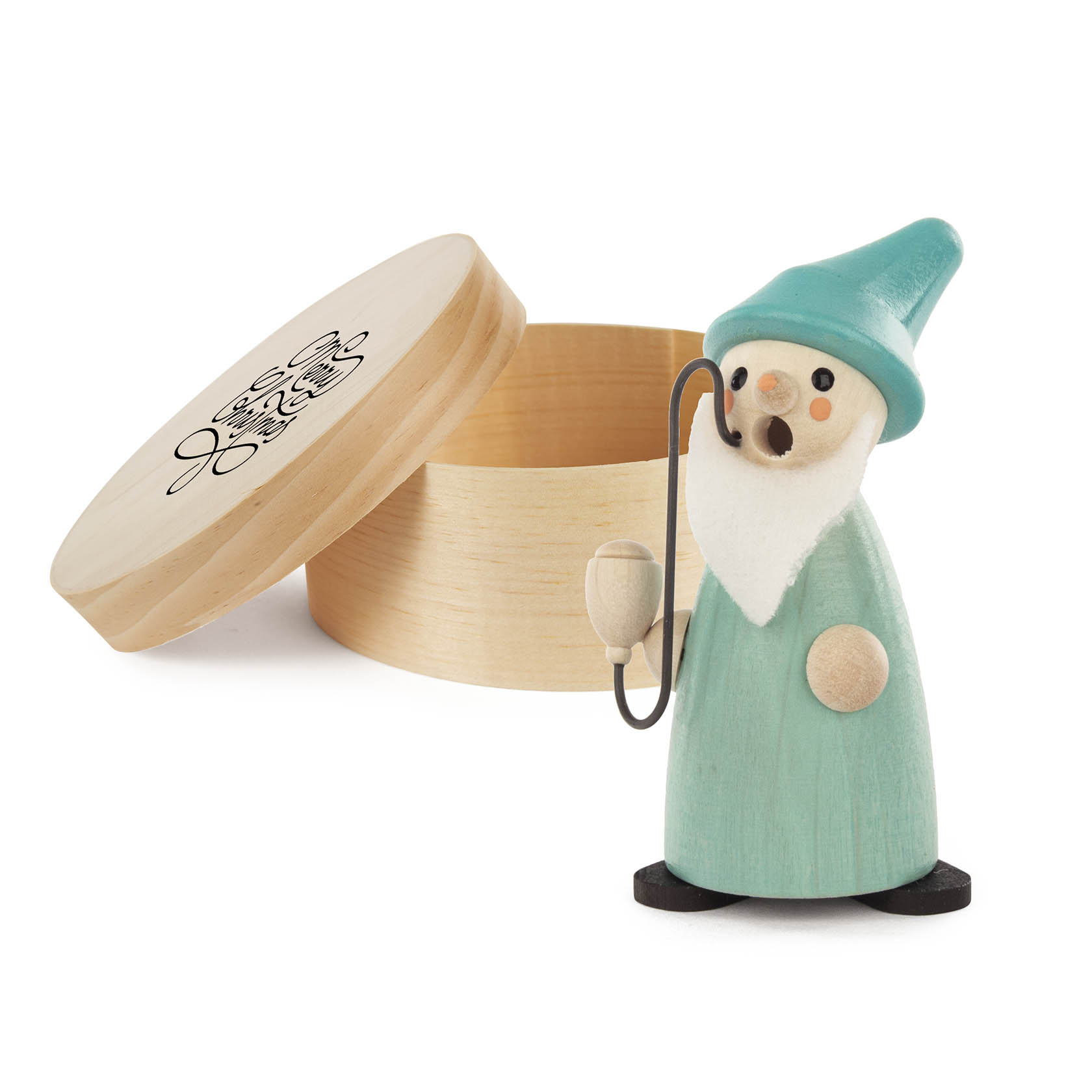 A small turquoise wooden incense gnome with a white beard and hat stands next to an open round wooden box with a gender-neutral figure illustration on the lid.