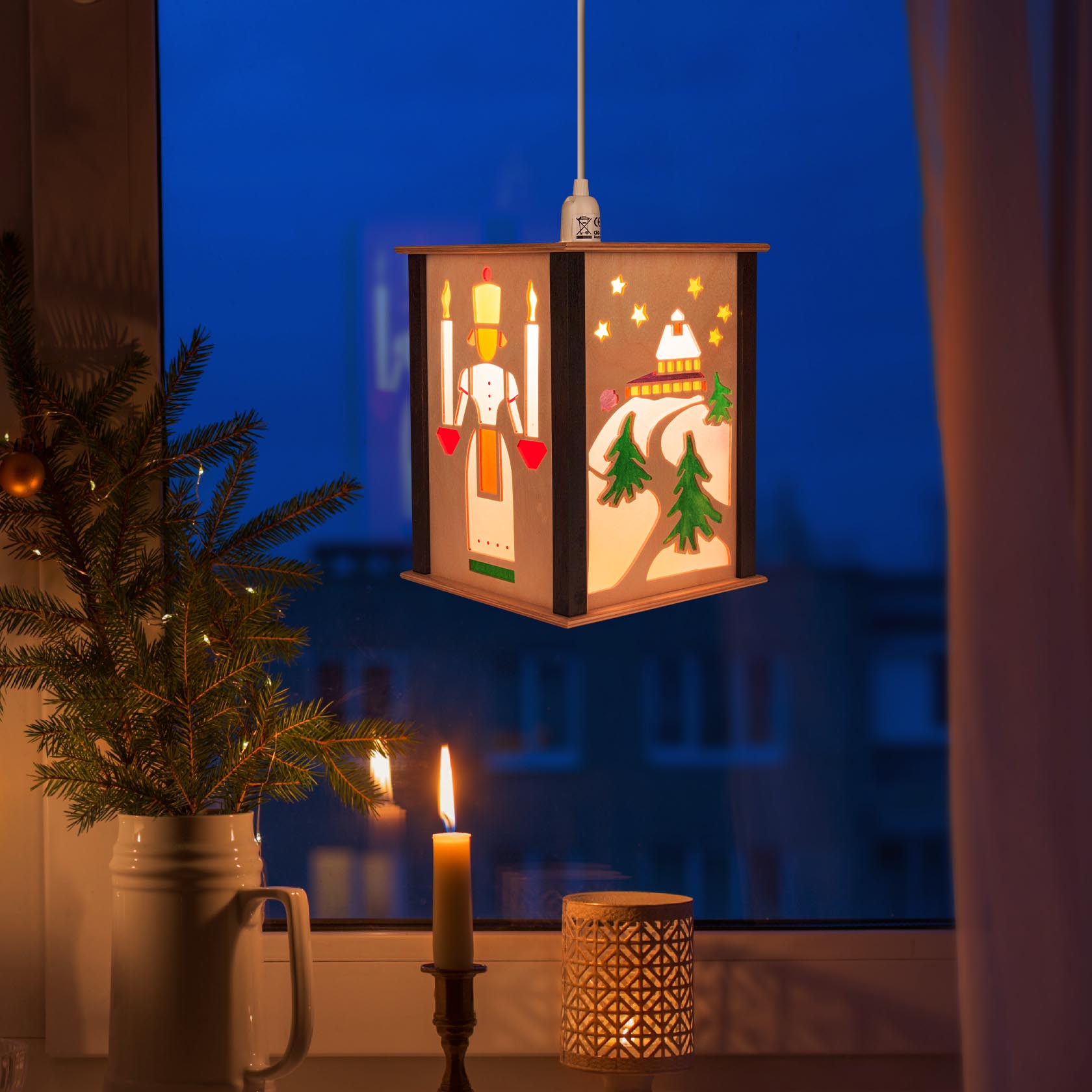 Weihnachtliche Laterne mit Motiven der Seiffener Kirche und einem traditionellen Nussknacker, aufgehängt an einem Fenster mit brennender Kerze.