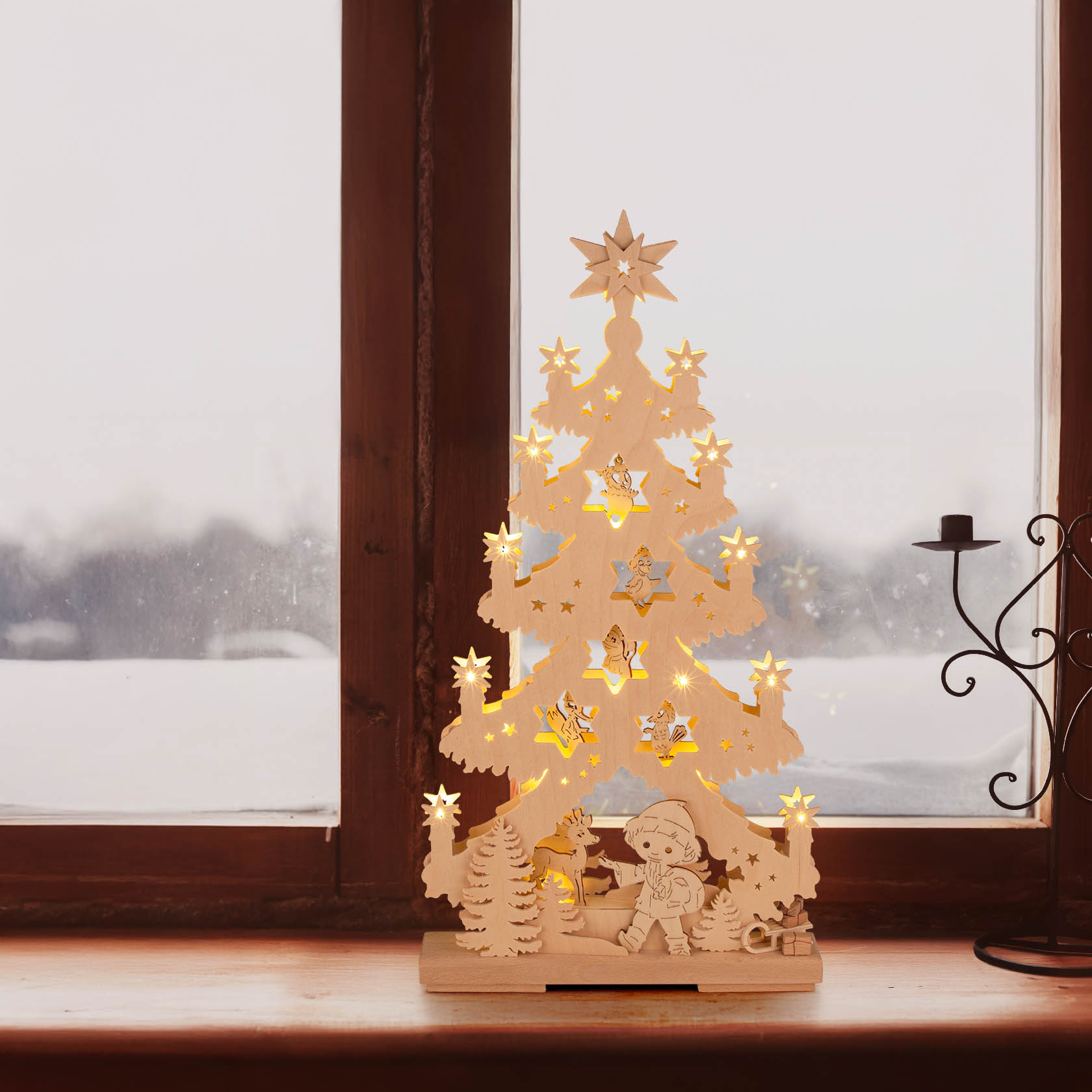 Holztanne mit beleuchtetem Sandmännchen und Waldmotiv, 10 LED-Lichter, auf Fensterbank vor verschneitem Fenster.