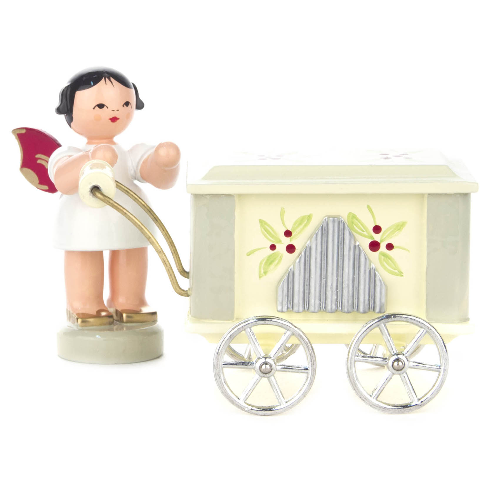A wooden angel figurine with red wings stands next to a decorative organ grinder. The angel is dressed in white, holding the organ's crank handle.