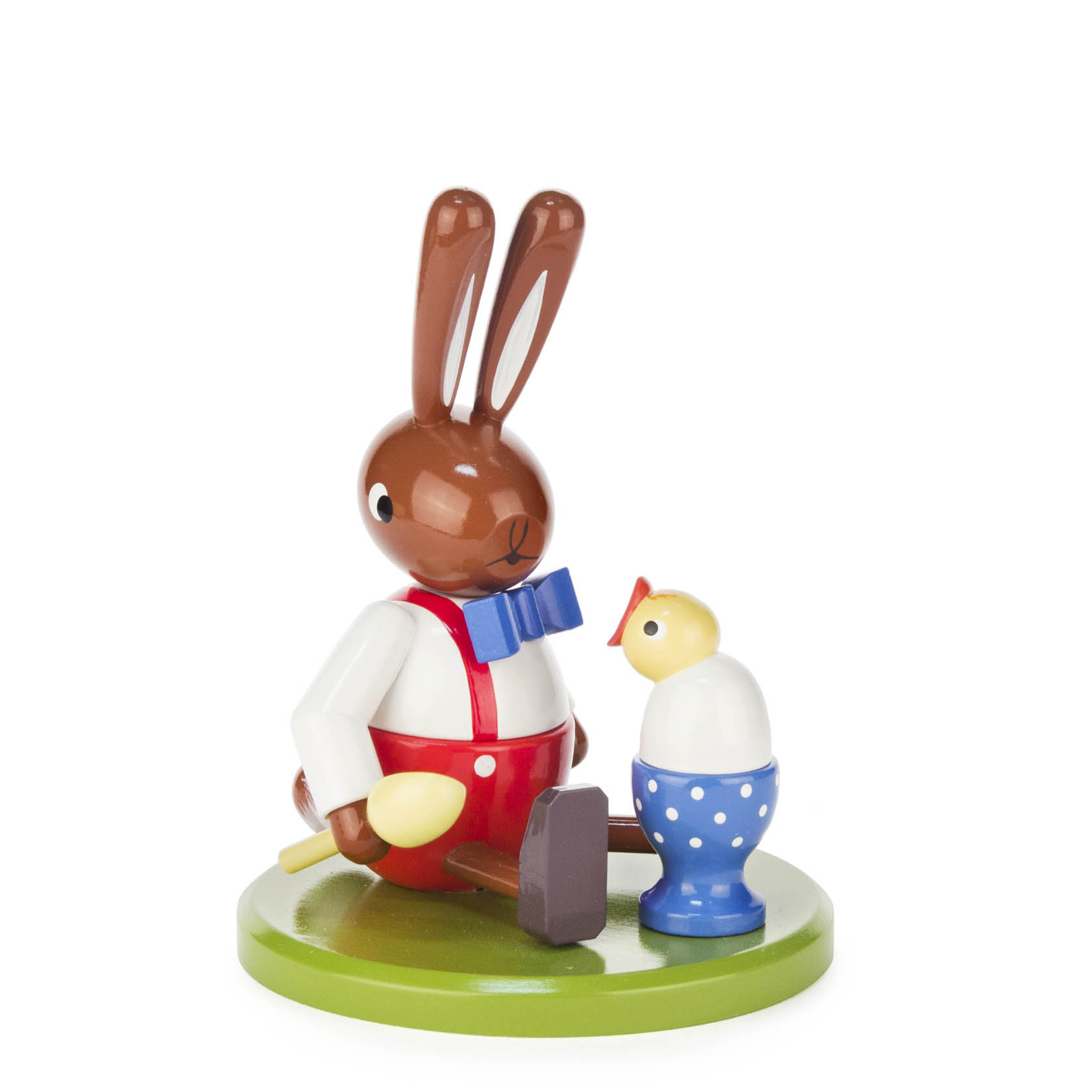 A wooden rabbit figurine sits with a yellow spoon in its paw next to a large blue polka dot egg cup, which has a small chick on top.