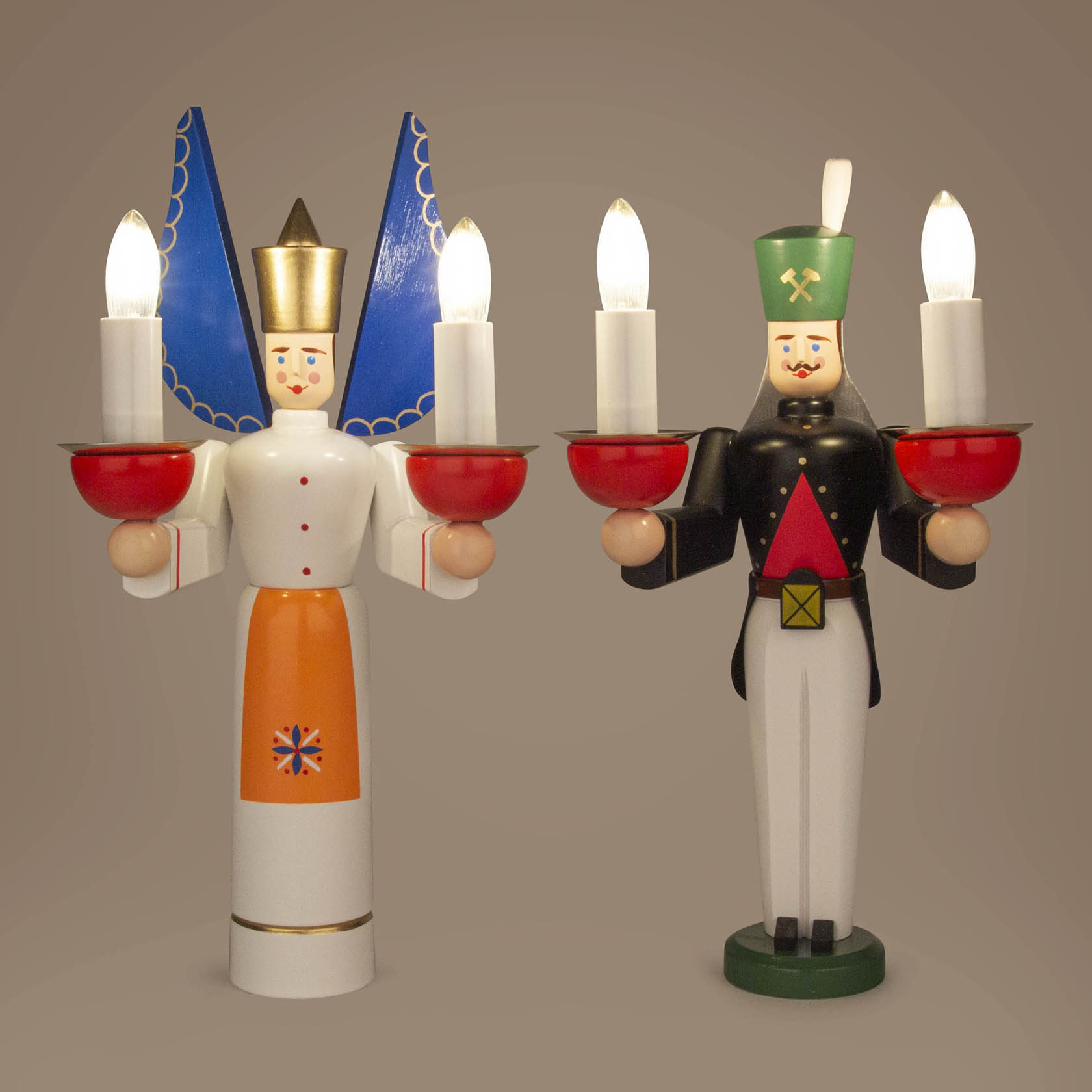 Ein Engel und ein Bergmann aus Holz, elektrisch beleuchtet. Der Engel trägt blaue Flügel und hält zwei rote Kerzenhalter, der Bergmann trägt grüne Mütze und hält ebenso Kerzenhalter.