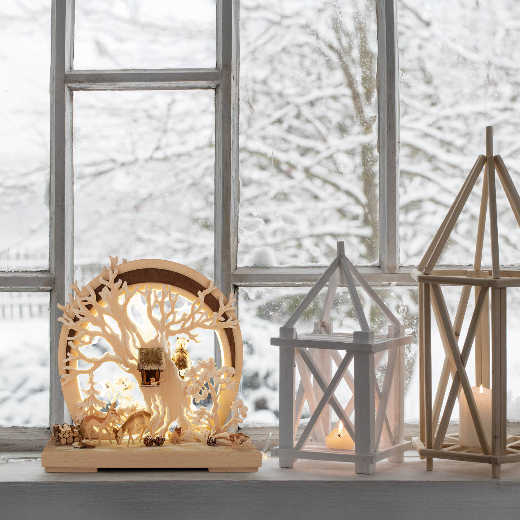 A decorative light display featuring woodland animals and frost with indirect LED lighting, placed on a windowsill with a snowy backdrop.