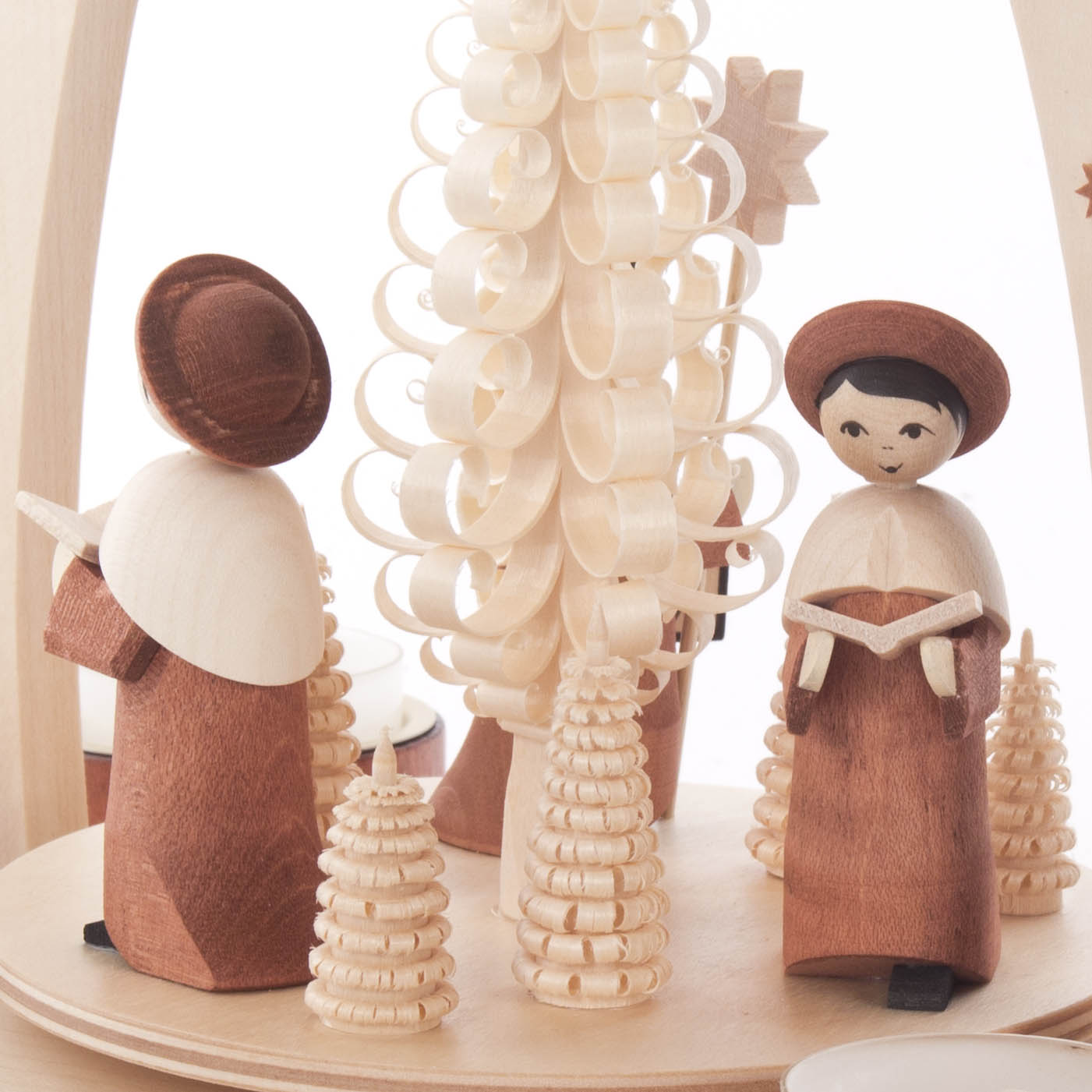 Zwei hölzerne Kurrendefiguren, ein Junge mit braunem Hut und ein Mädchen mit schwarzen Haaren, stehen um einen filigranen Holzbaum.