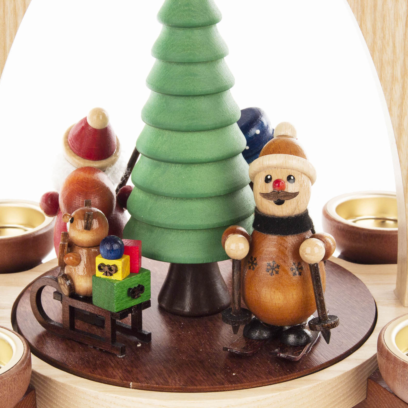 Holzpyramide mit Weihnachtsmann und Schneemann, beide bunt bemalt, um einen grünen Holzbaum. Ein Schlitten mit Geschenken und Teelichthalter sichtbar.
