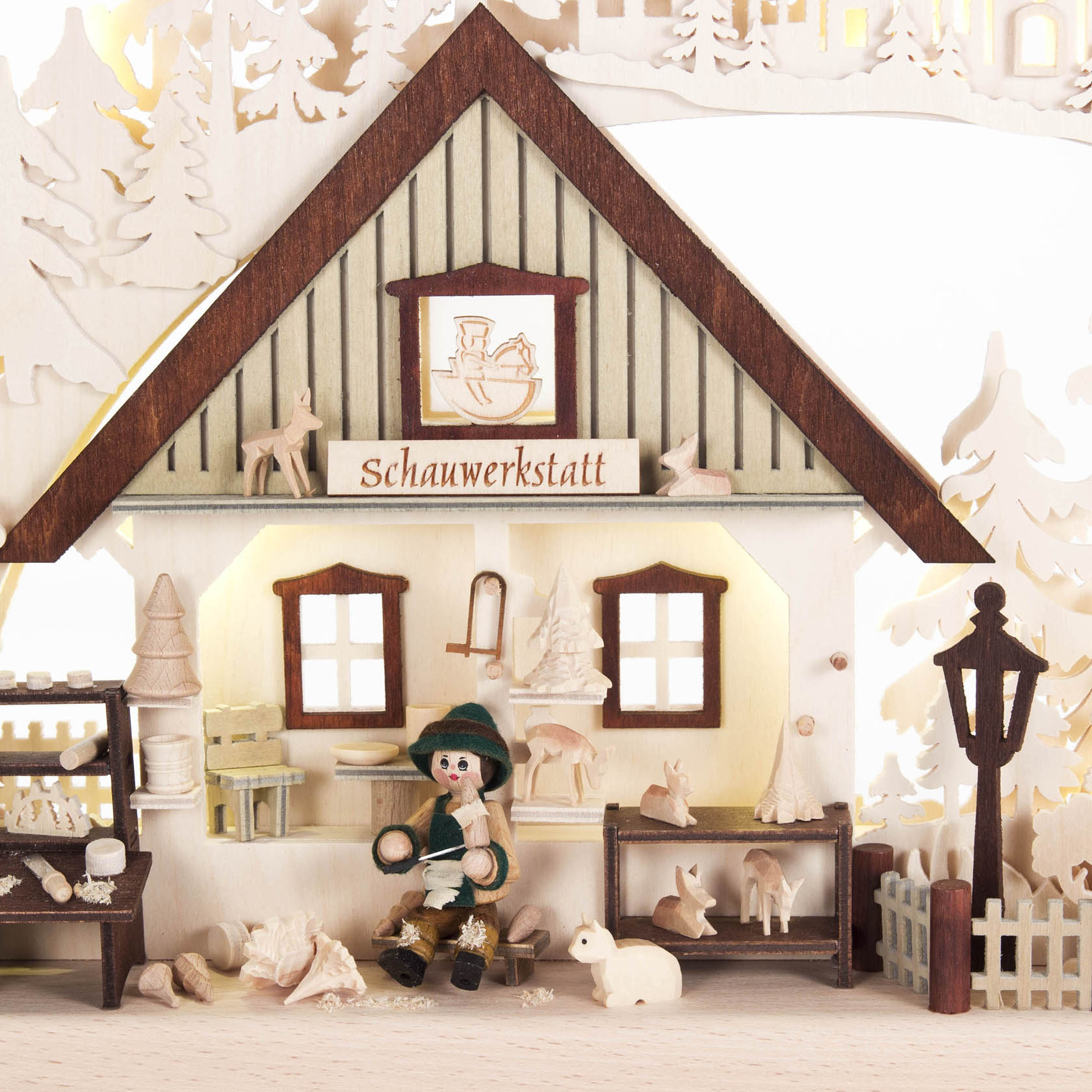 Miniature woodworking shop scene with a figure carving at a bench, surrounded by wooden animal figures, under an arched display with indirect light.