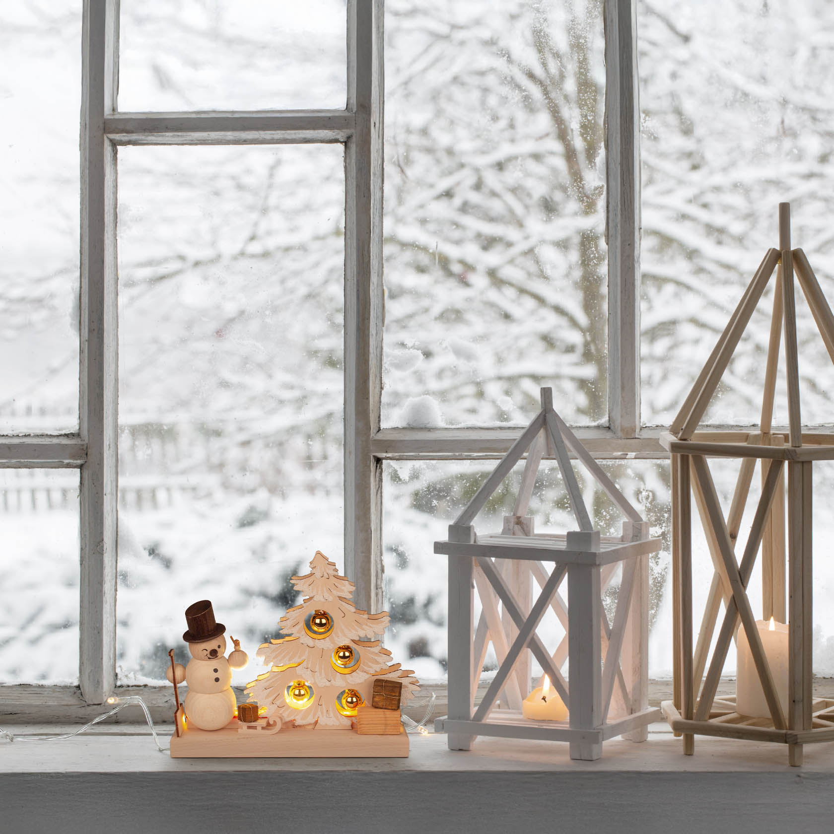 Ein kleiner beleuchteter Tannenbaum aus Holz mit einem Schneemann und einer Schaufel dekoriert. Der Baum hat warm leuchtende LEDs.